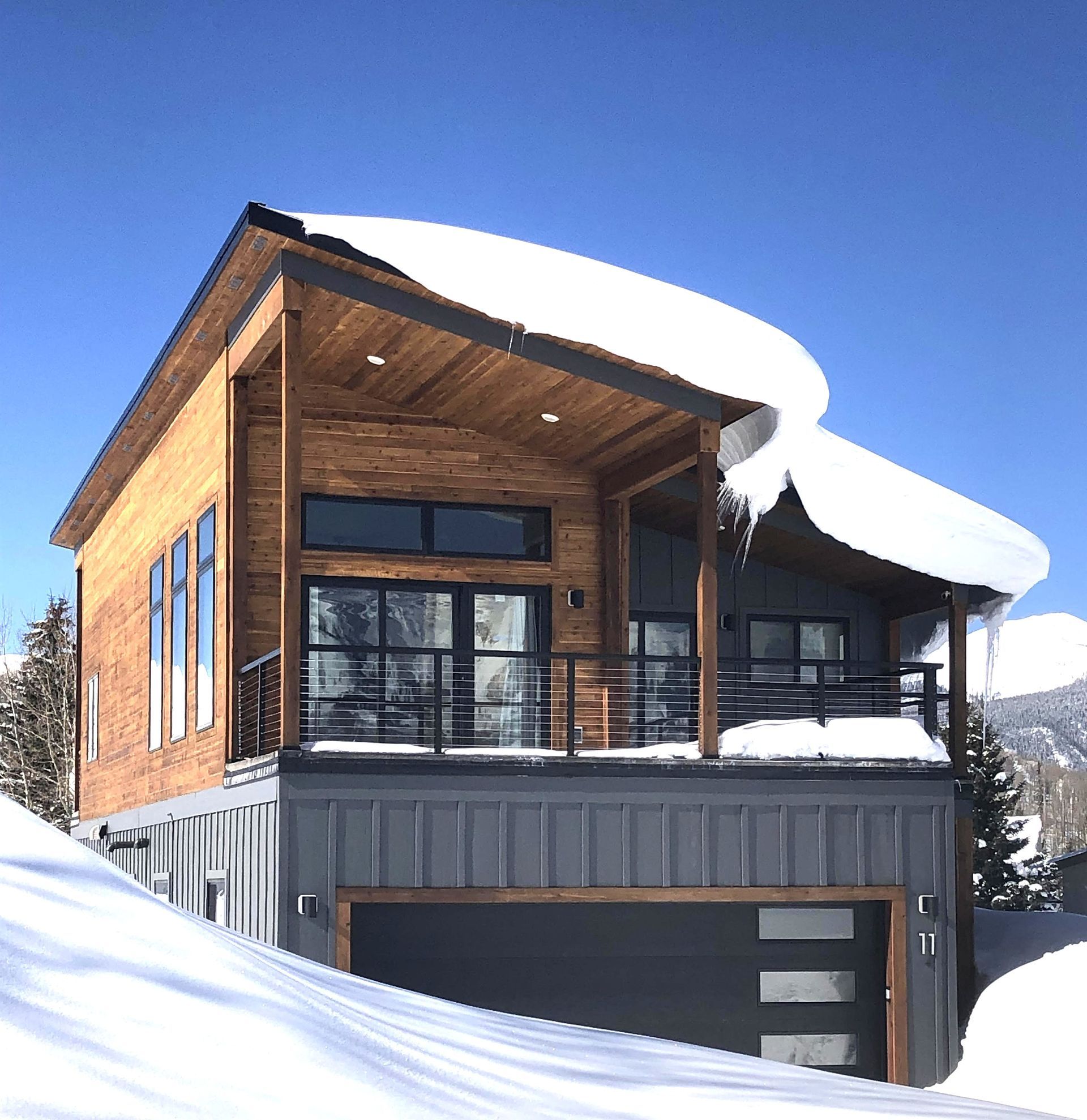 Modern chalet-style house with wood siding and a snow-covered roof in a snowy mountain setting
