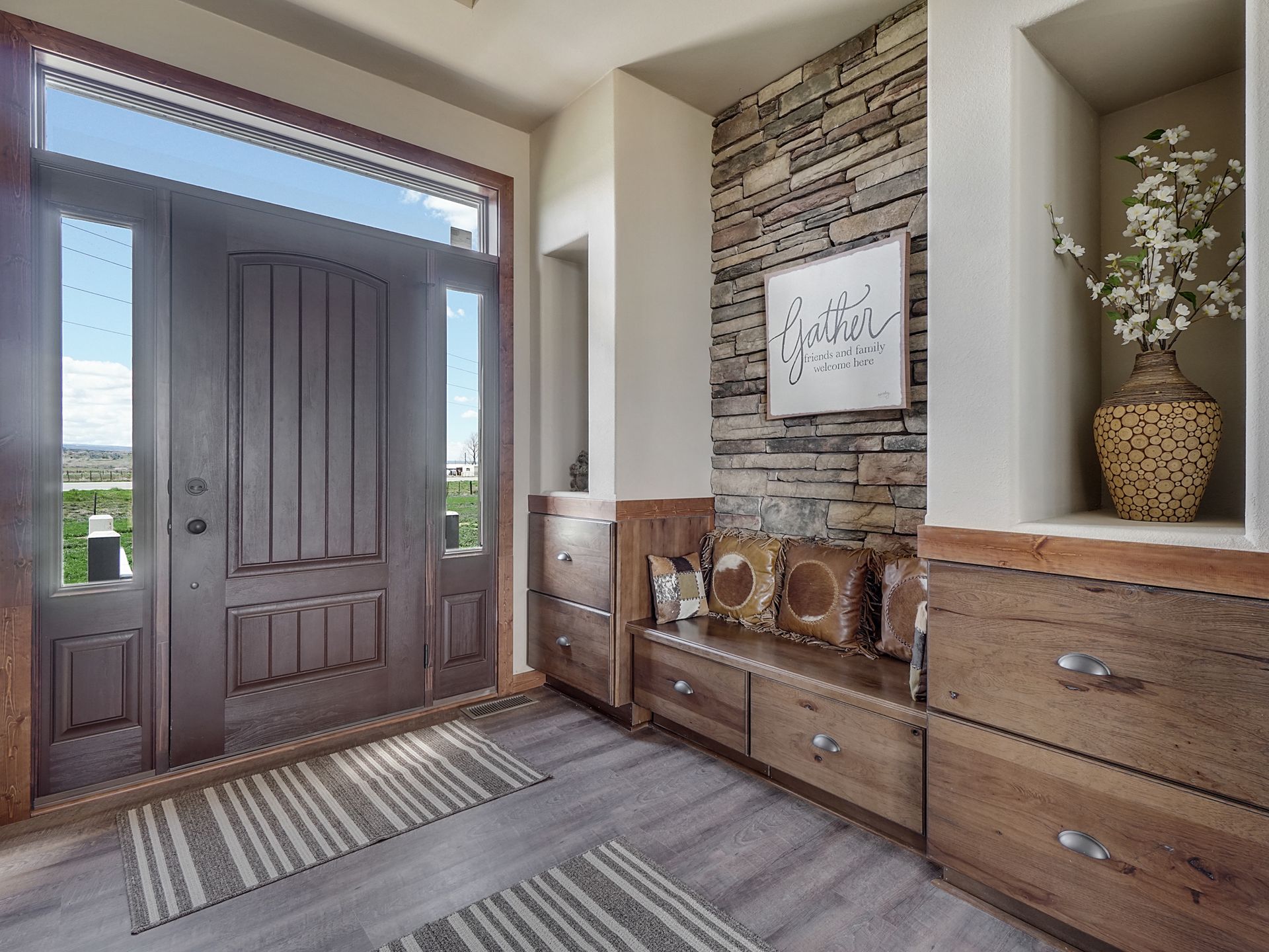 Entryway with dark front door, wood console, woven rug, and stone accent wall.