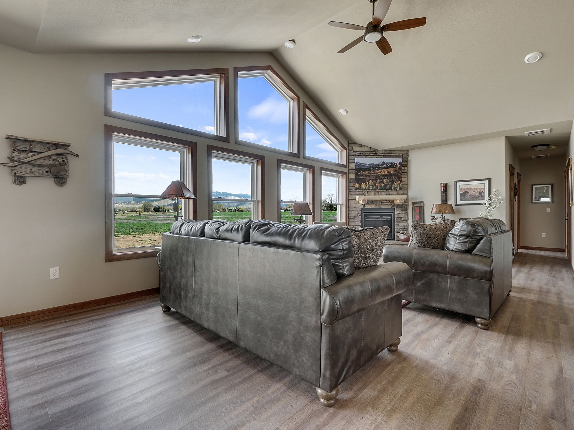 Spacious living room with vaulted windows, gray sofas, wood floor, and ceiling fan.