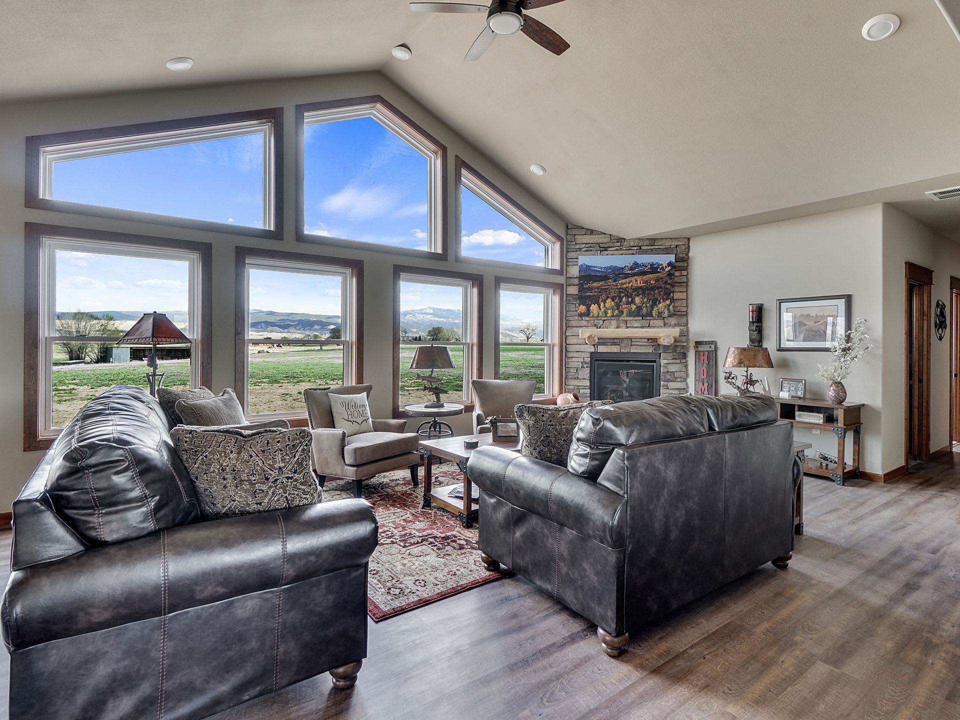 Bright living room with vaulted windows, black leather sofas, and countryside views