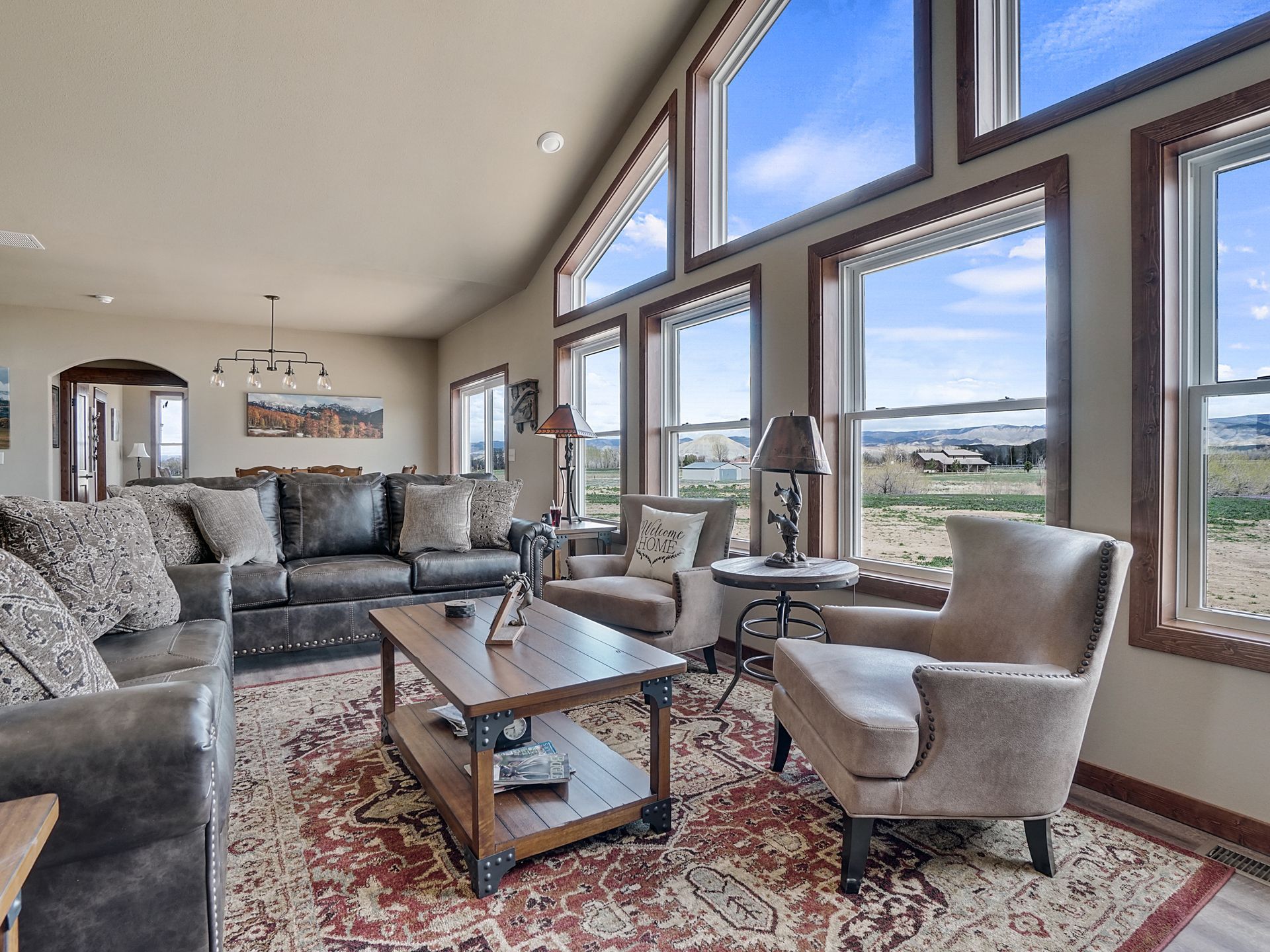 Bright living room with large windows, gray seating, and a patterned rug overlooking a scenic view.