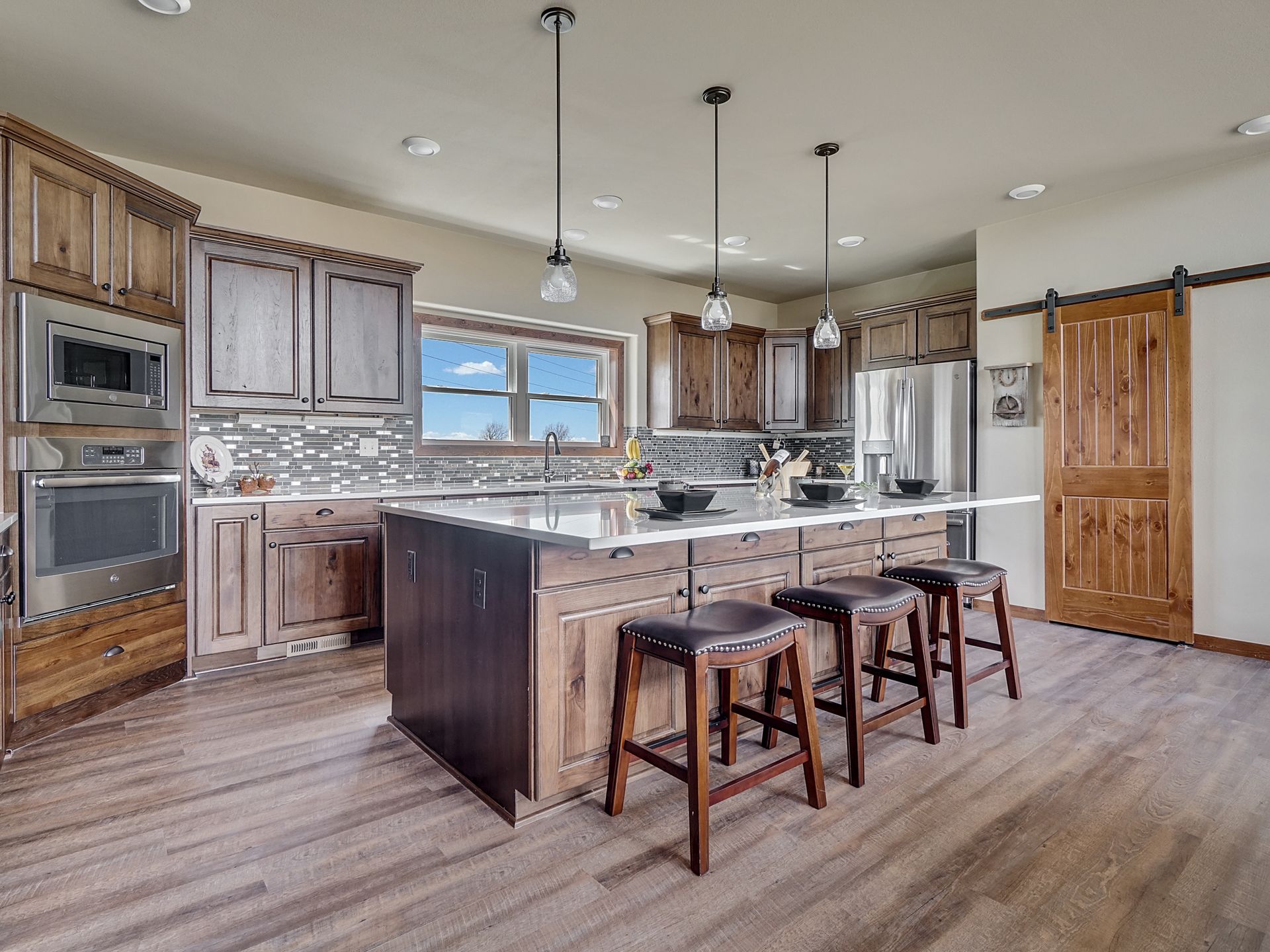 Spacious modern kitchen with wood cabinets, large island, and three stools under pendant lights.