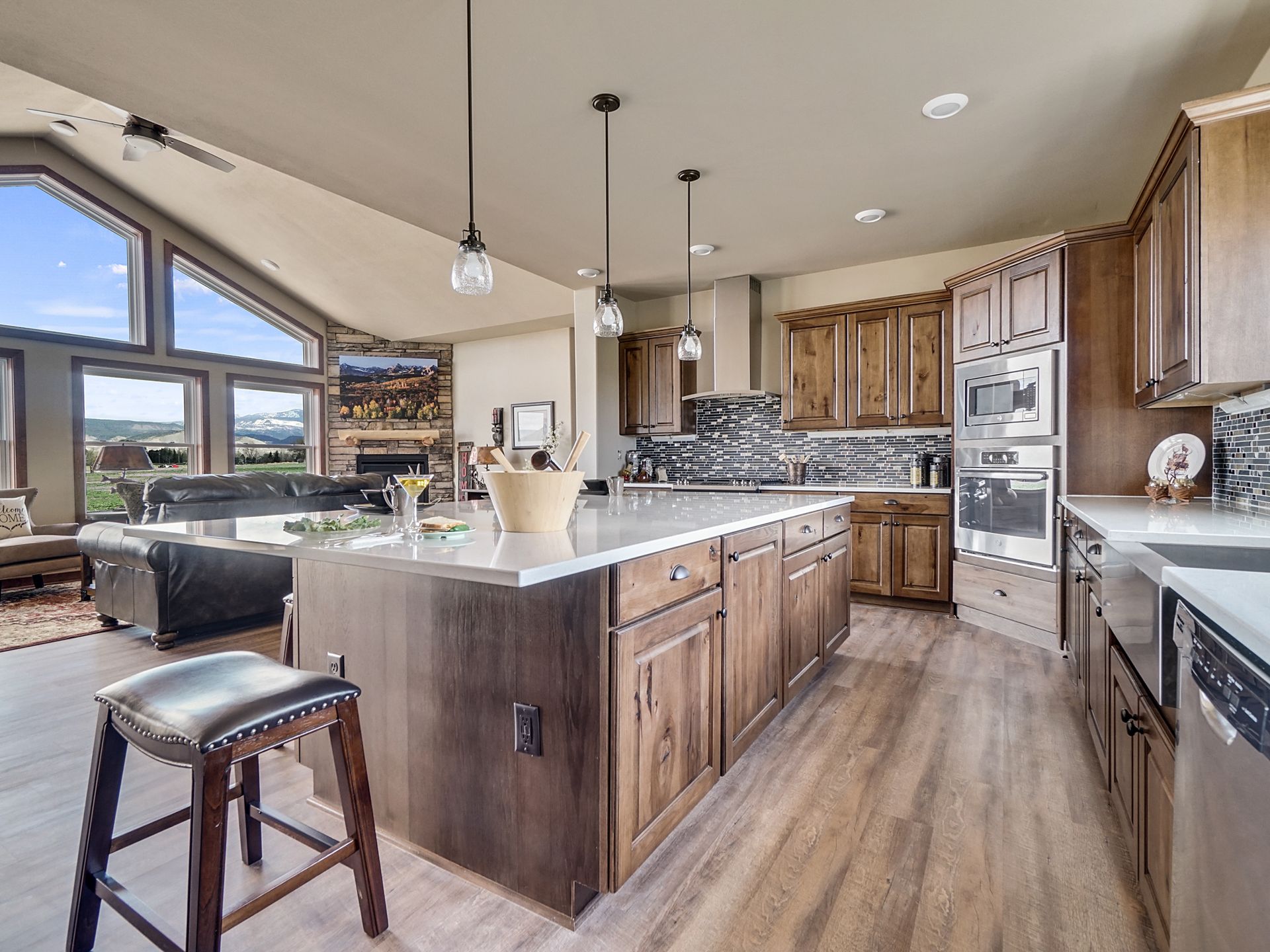 Modern open kitchen with wood cabinets, white island, bar stool, and large windows overlooking a bright living area
