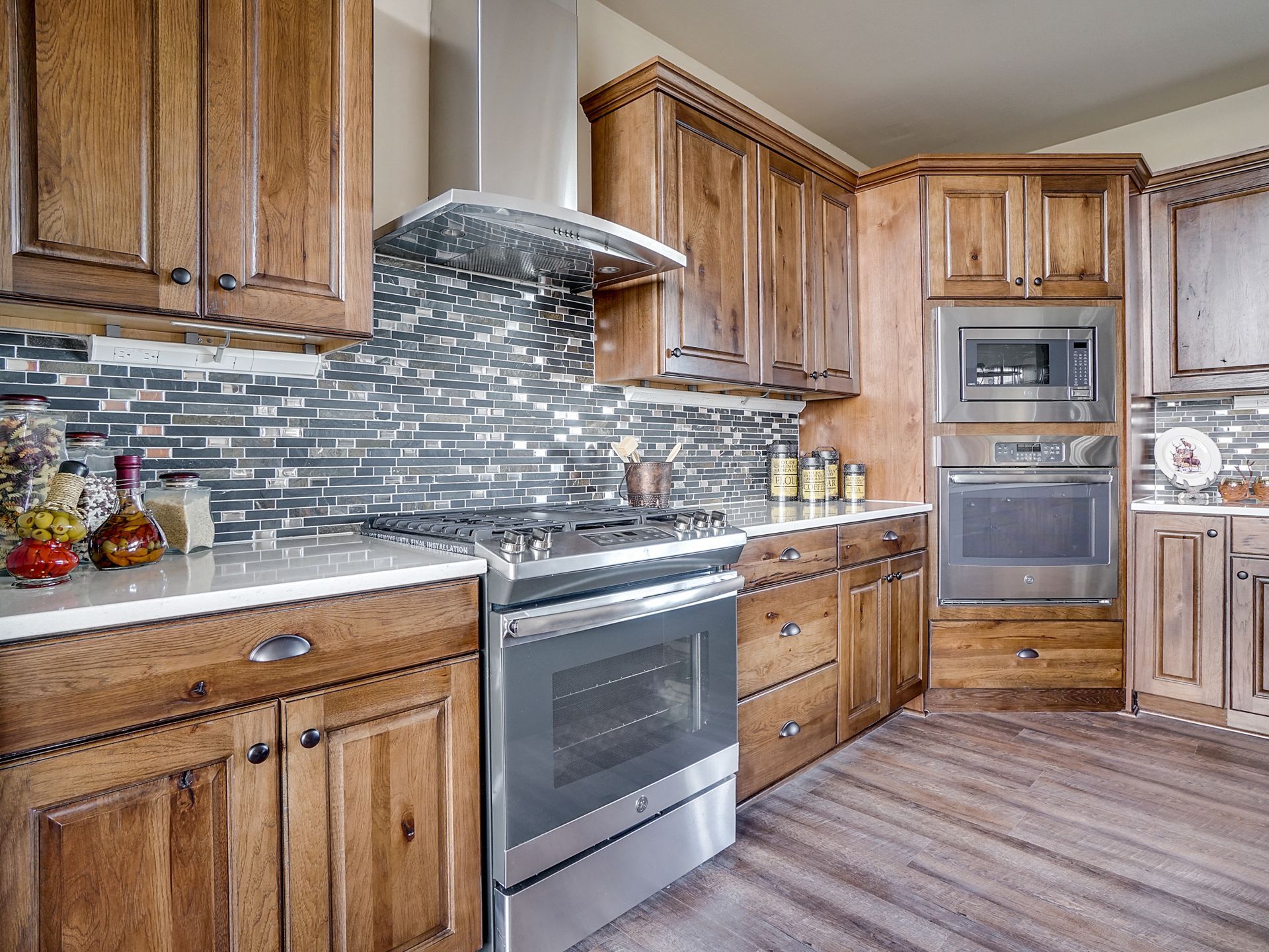 Modern kitchen with wooden cabinets, stainless steel appliances, mosaic backsplash, and wood-look flooring