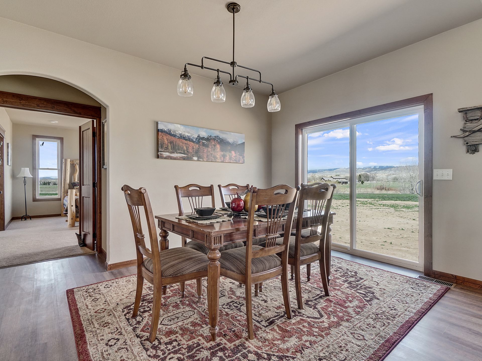 Dining room with wooden table and chairs, patterned rug, and large sliding glass door overlooking a landscape.