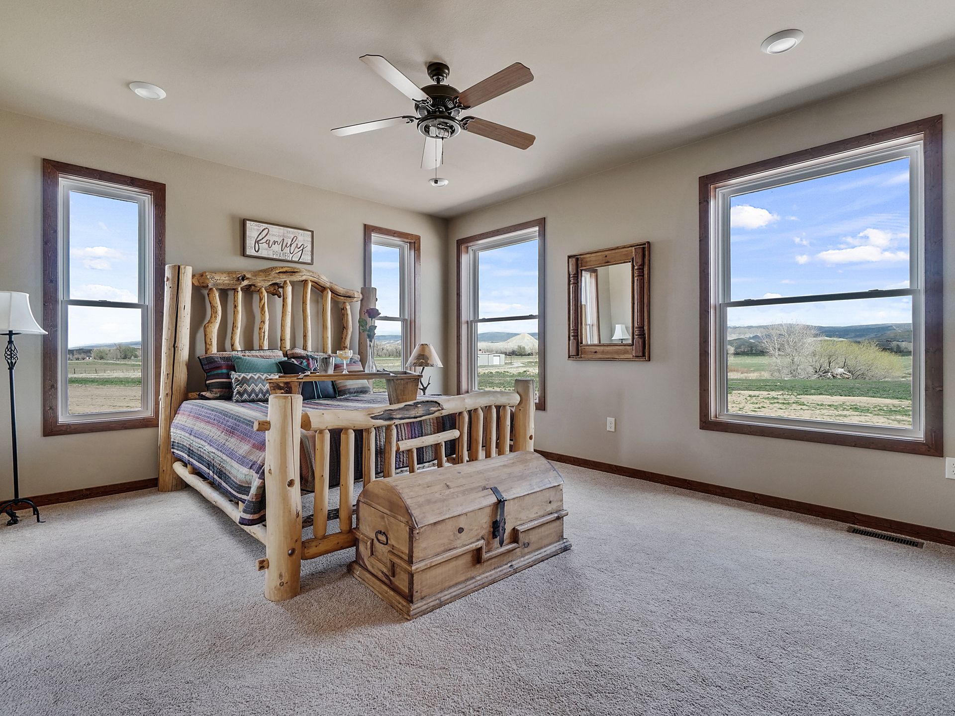 Bedroom with a bed, wooden chest, and large windows overlooking a grassy landscape.