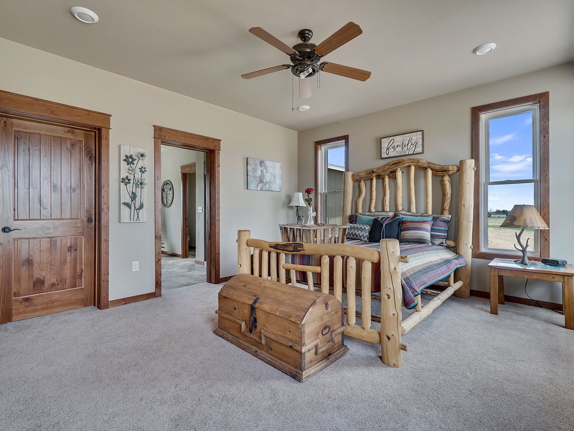 Spacious bedroom with a wooden bed, chest, carpet, and large windows under a ceiling fan