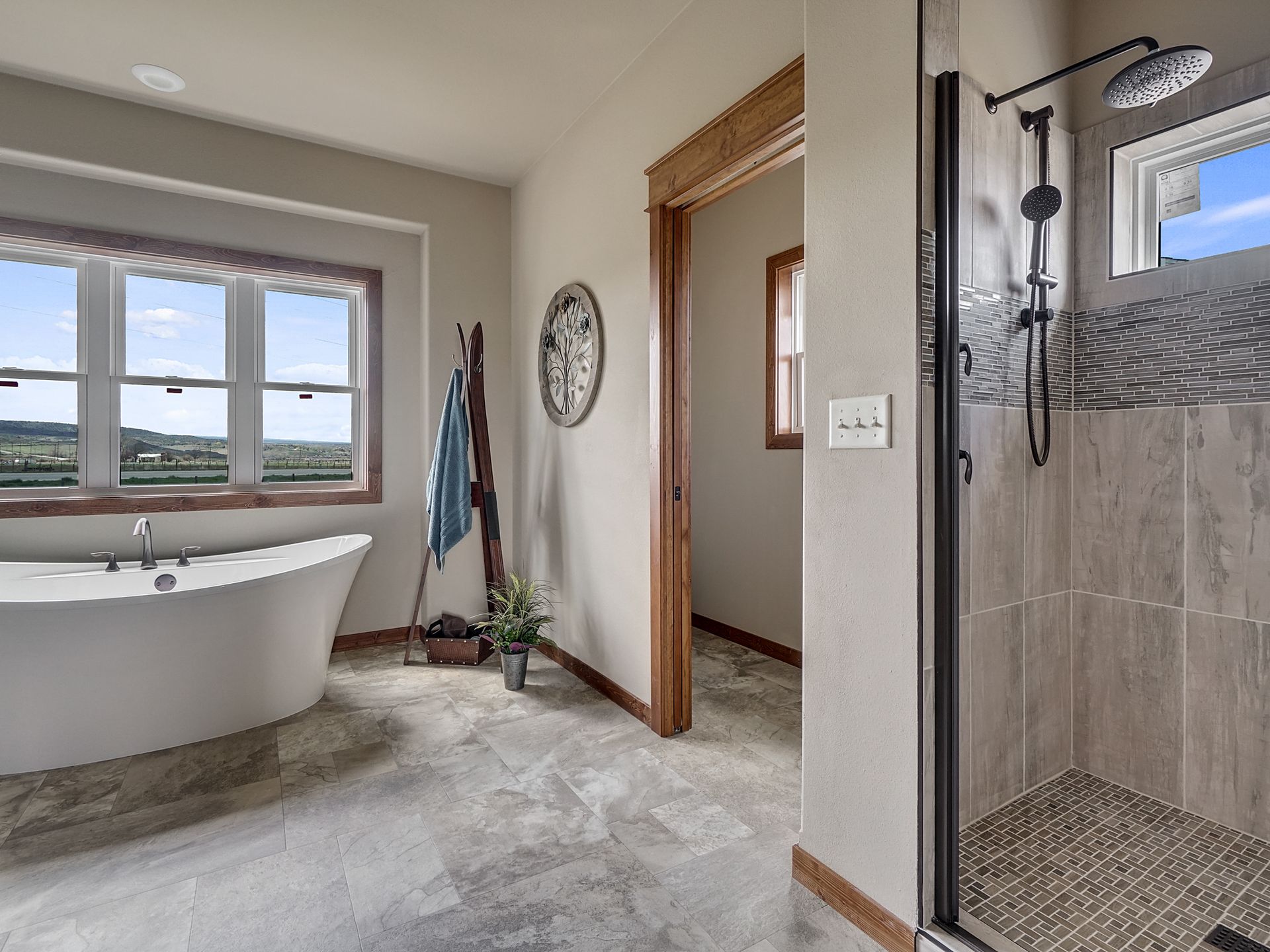 Bathroom with freestanding tub, walk-in shower, and large window overlooking open fields.