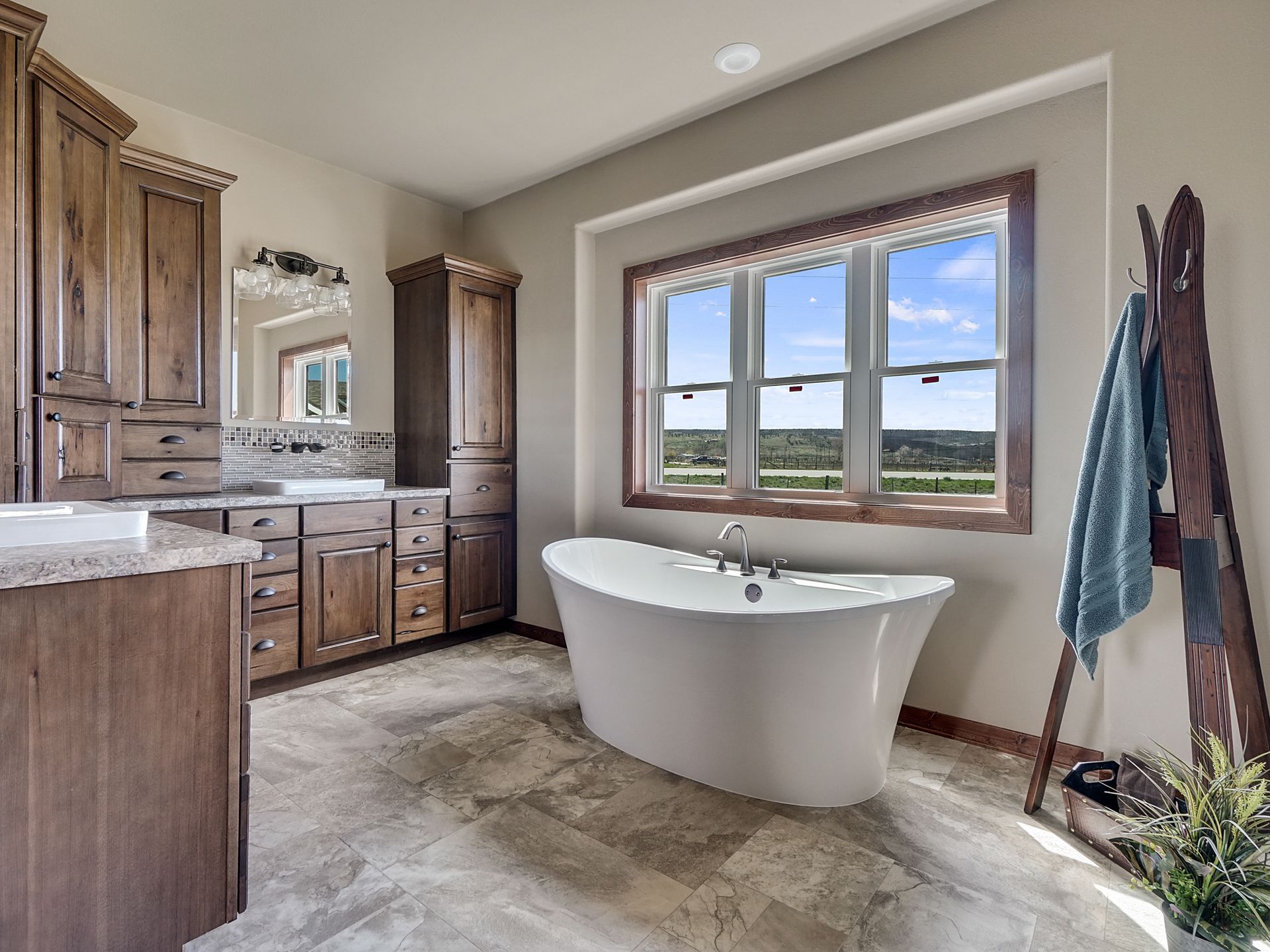 Spacious bathroom with wood cabinets, freestanding tub, and large window overlooking the outdoors
