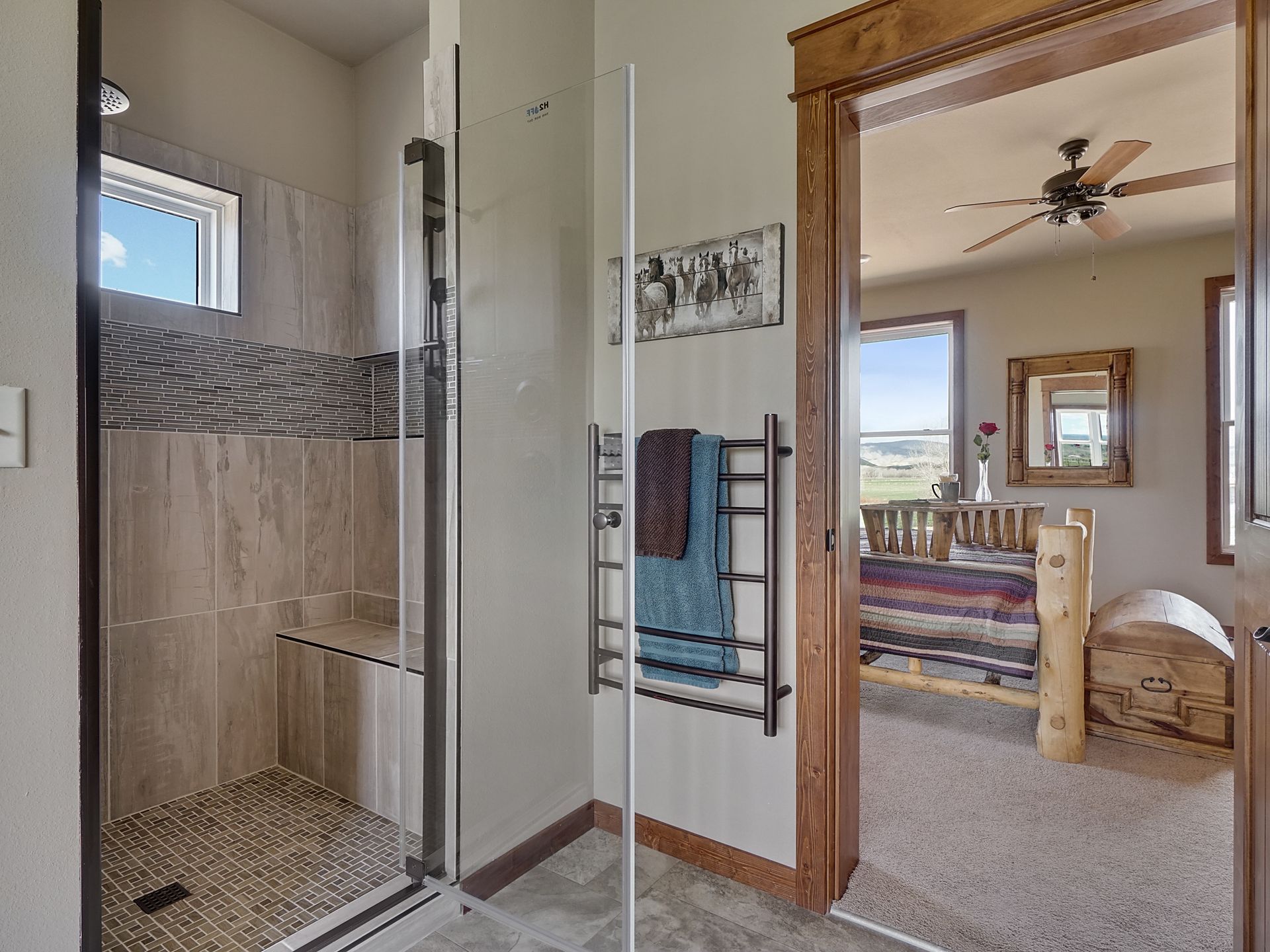 Bathroom with tiled walk-in shower and a doorway leading to a carpeted bedroom with mirror and ceiling fan