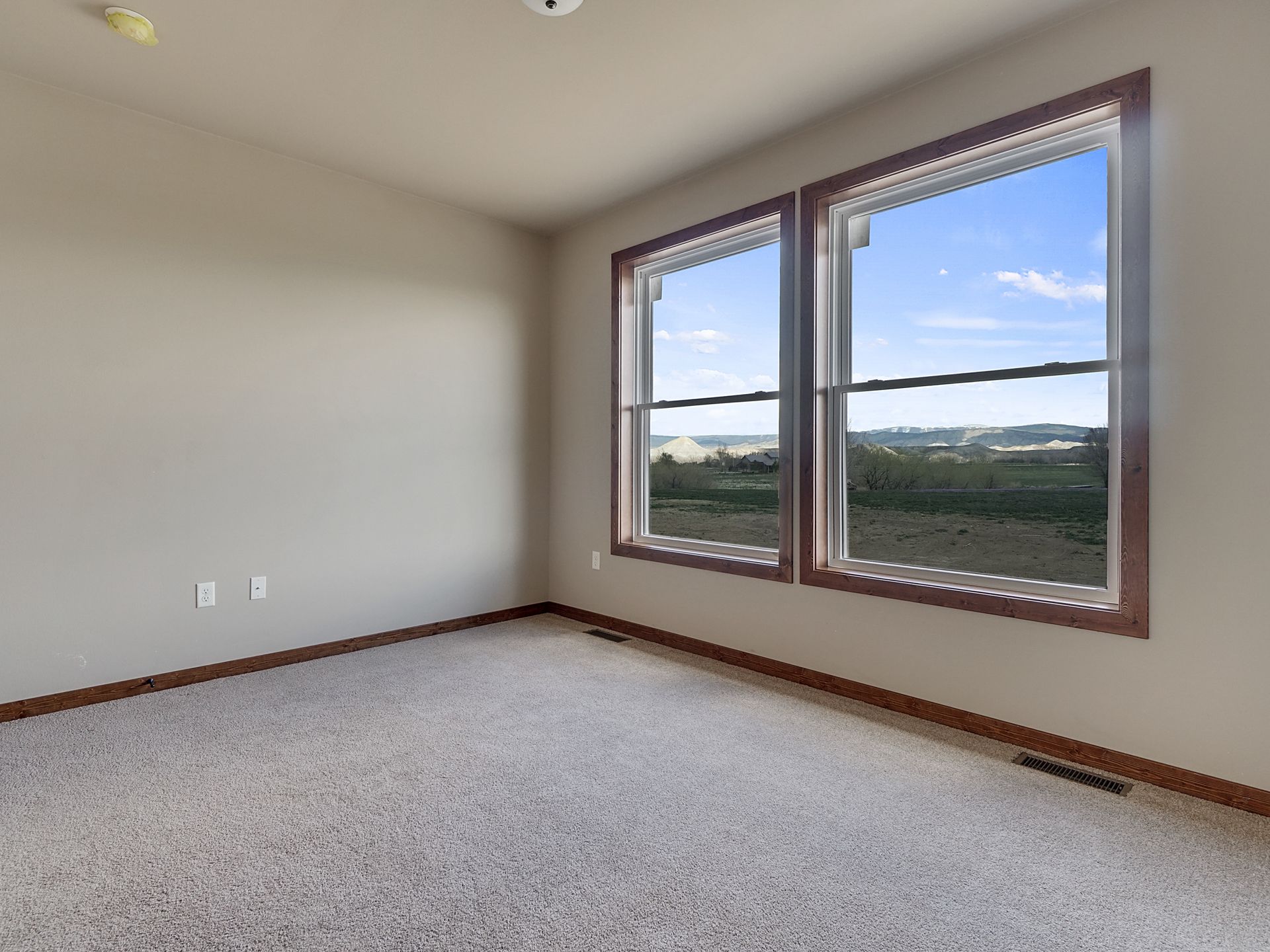 Empty carpeted room with beige walls, two windows, and a view outside