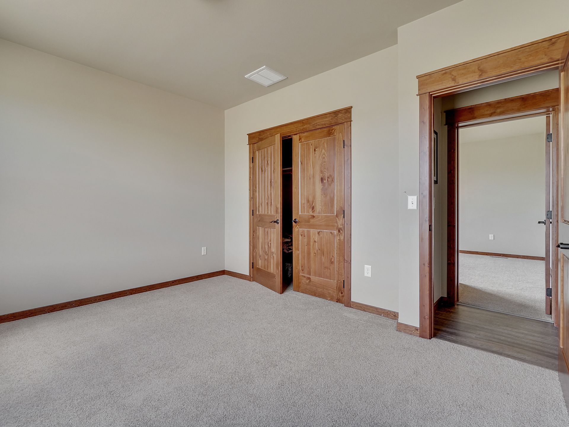 Empty beige bedroom with carpet, wooden double doors, and an open doorway to a closet.