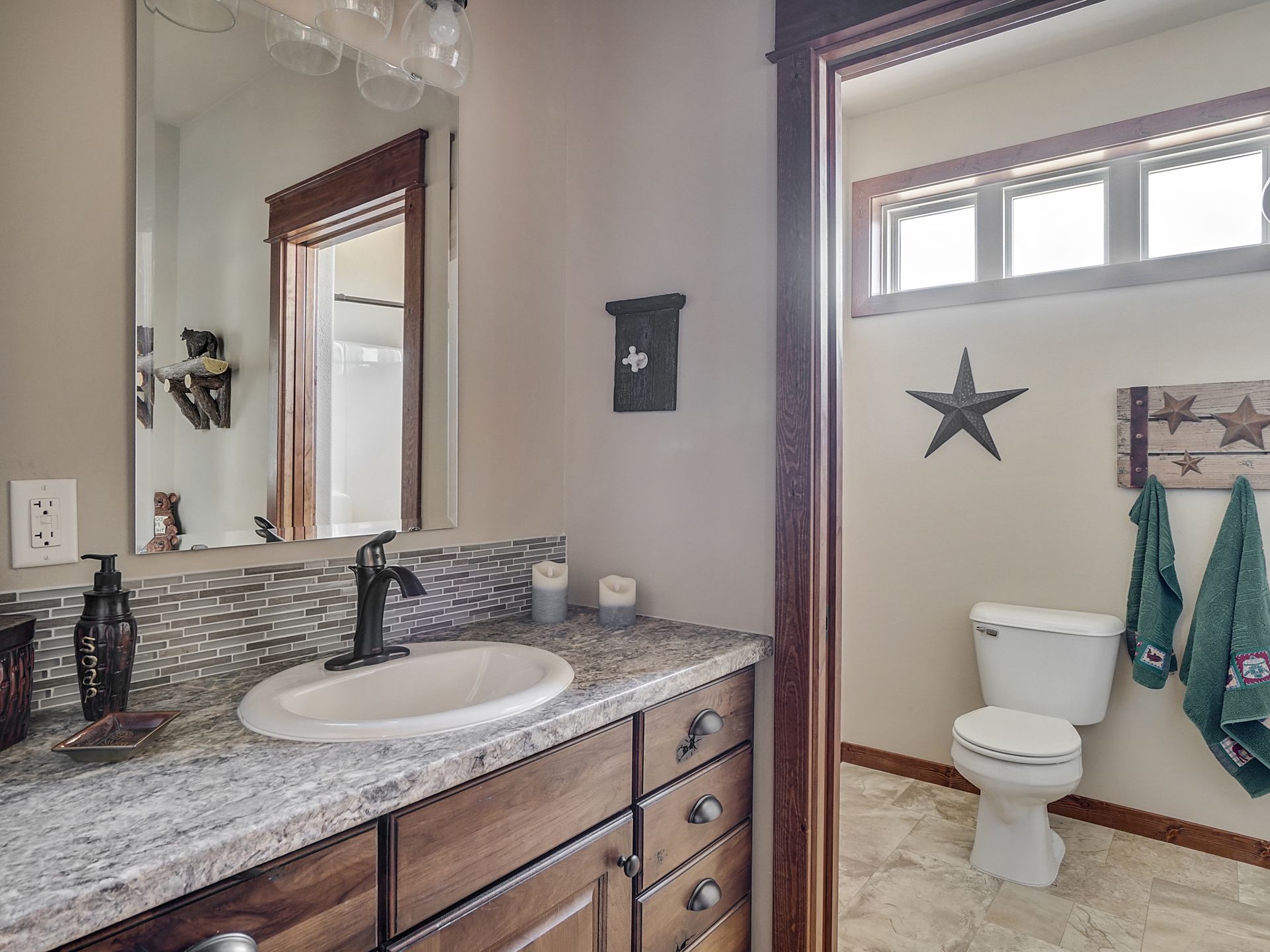Granite bathroom vanity with mirror and sink beside a toilet, towel rack, and star wall decor