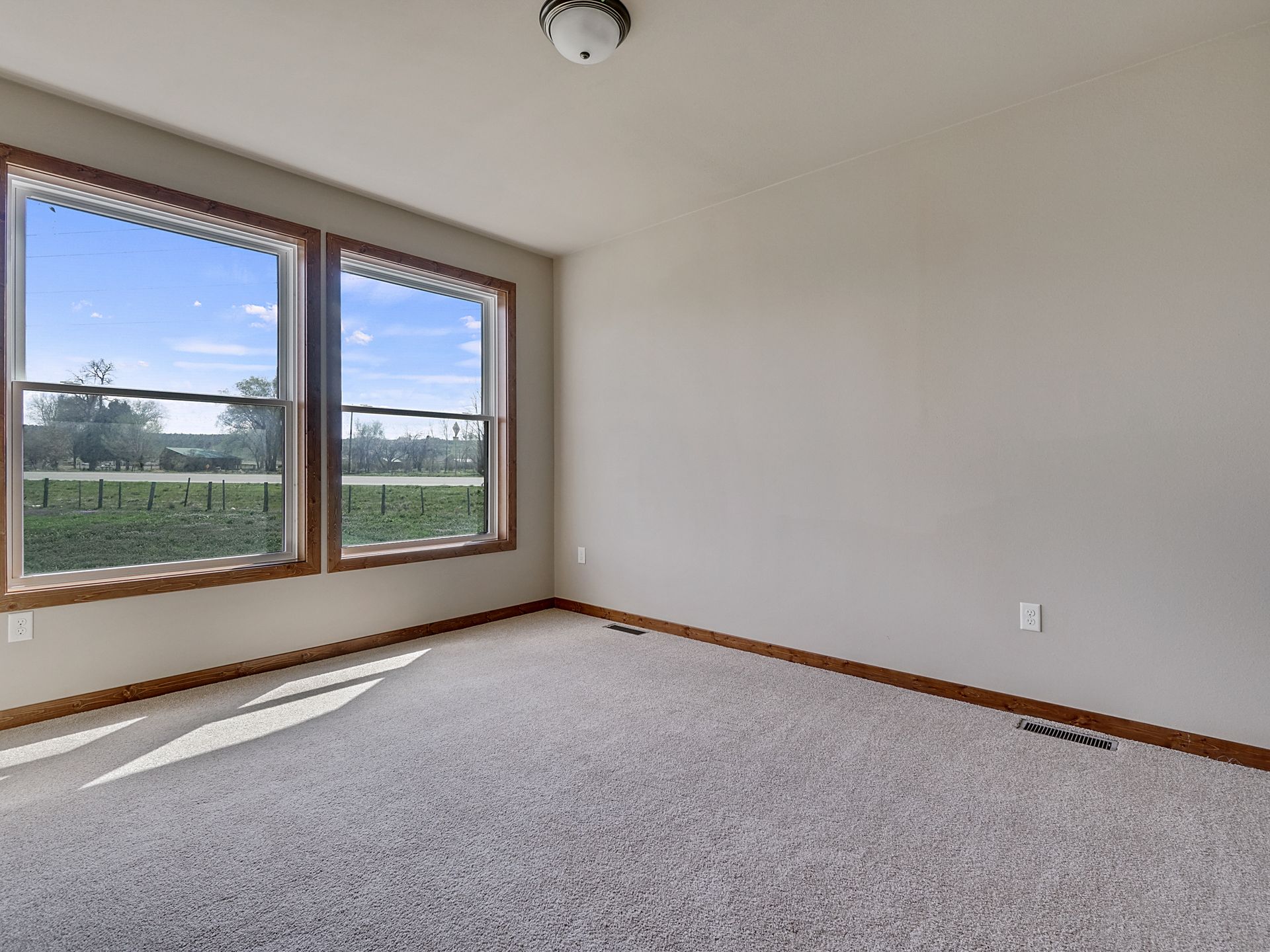 Empty beige bedroom with carpet, large corner windows, and a view of green fields outside