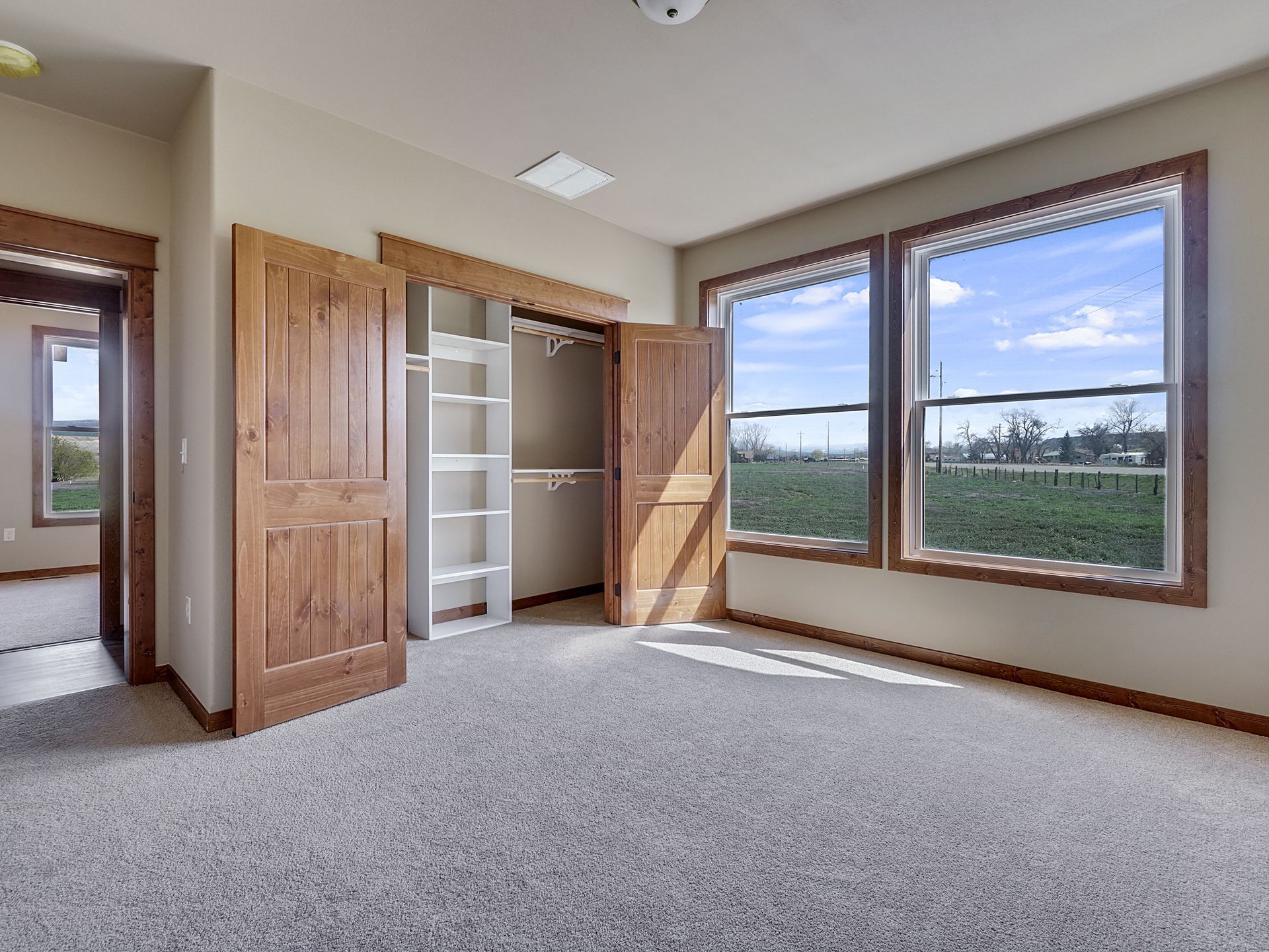 Empty carpeted bedroom with large windows and an open built-in closet.