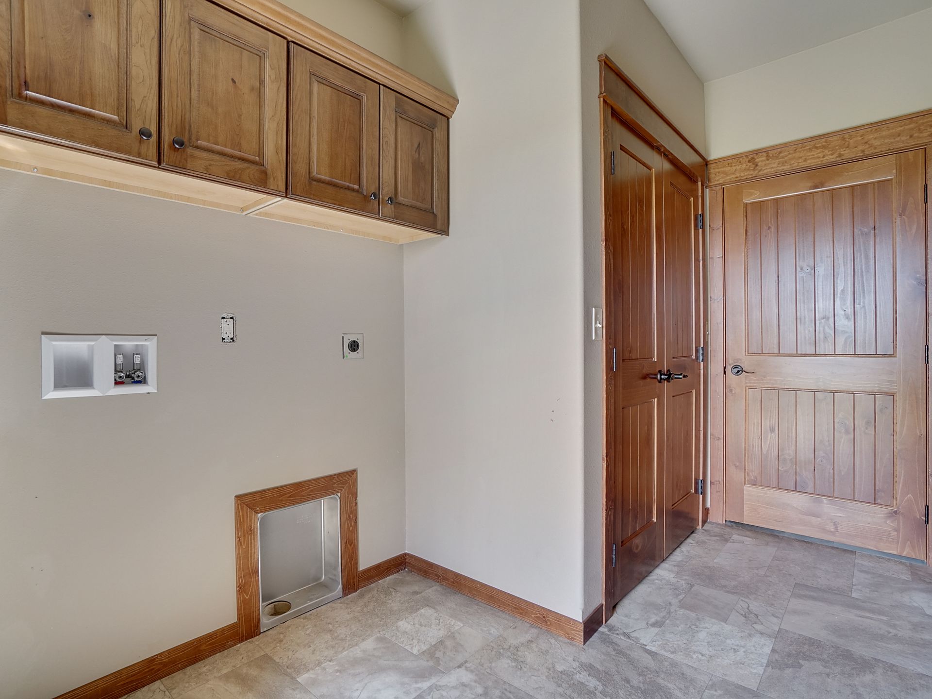 Empty laundry room with wood cabinets, hookups in the wall, and double wooden closet doors.