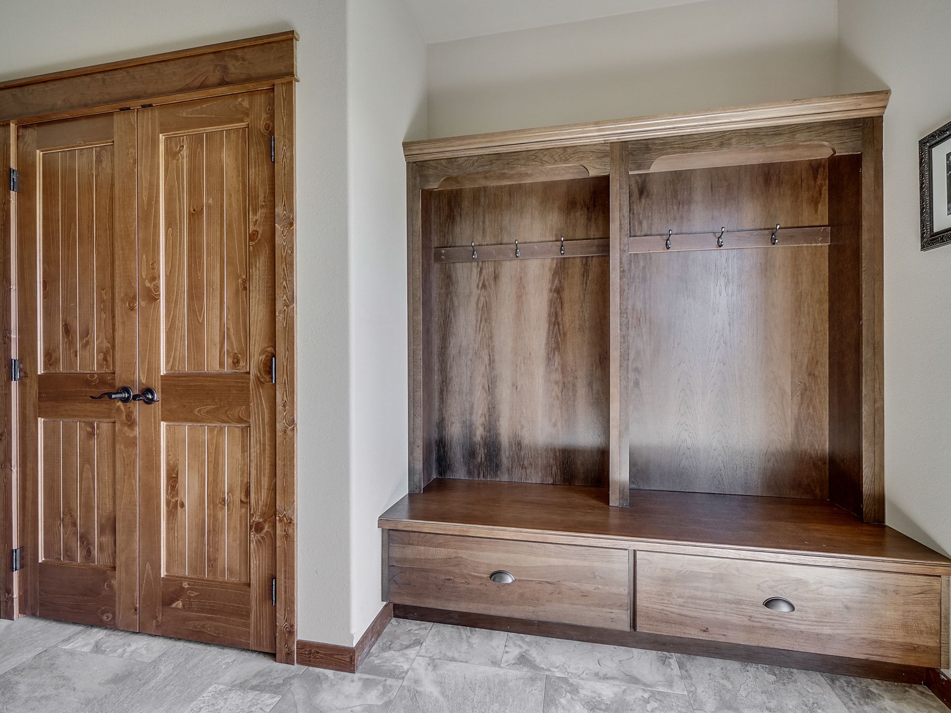 Wooden built-in coat and storage nook beside a matching double-door closet in a beige hallway