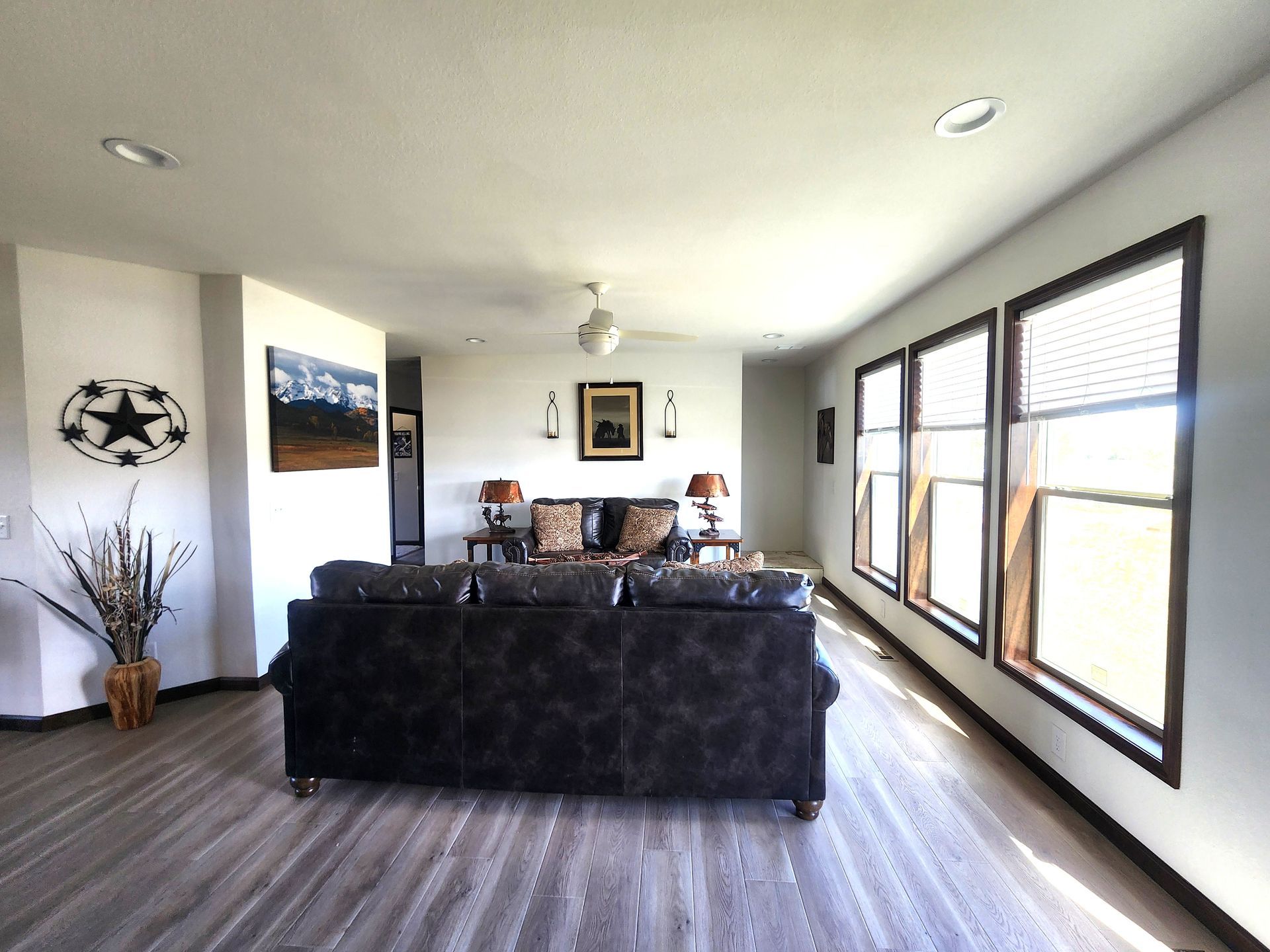Bright living room with a large black sofa, wall art, and sunlight from windows on the right.