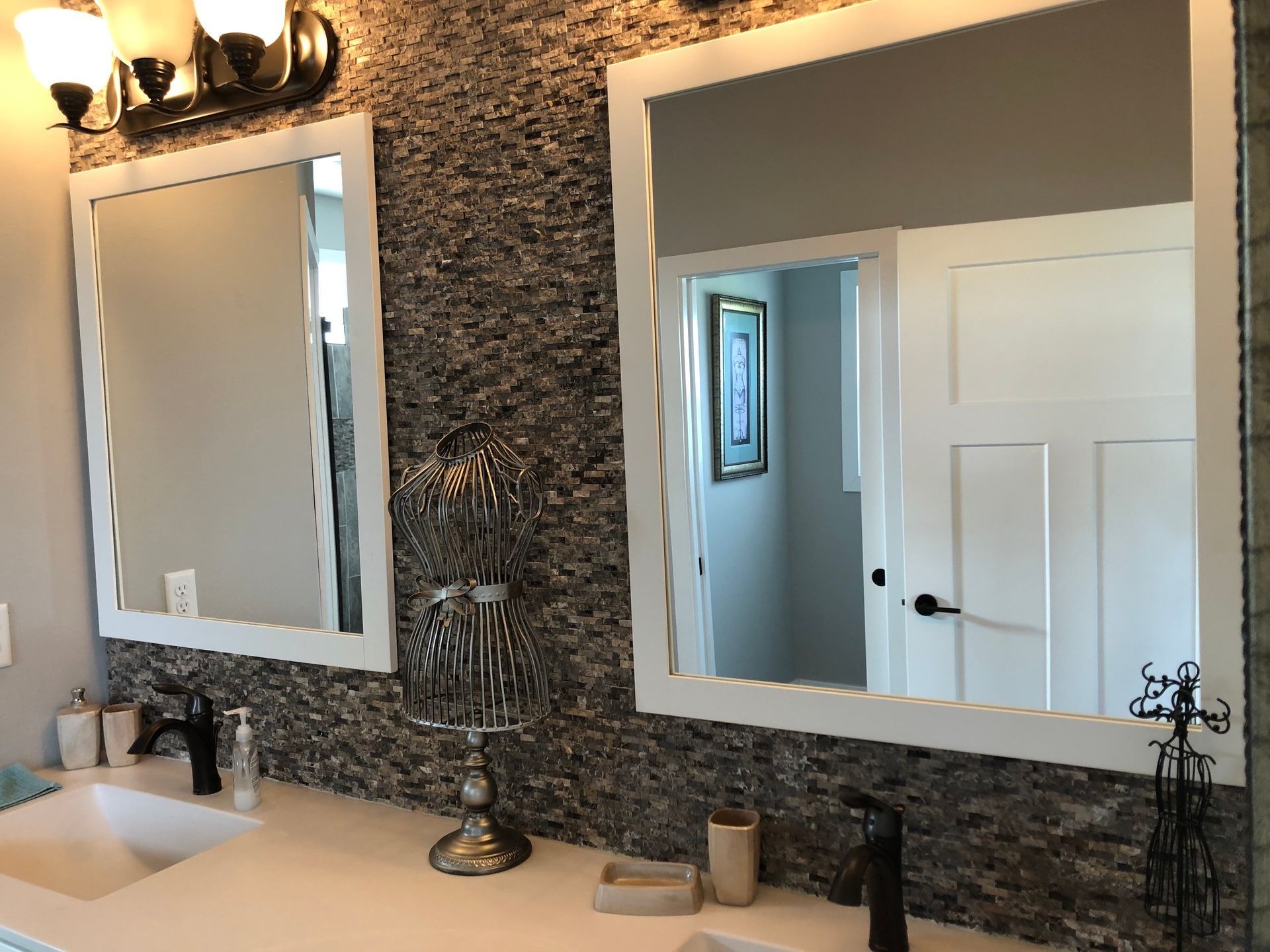 Bathroom vanity with two mirrors, sink, and granite countertop against a stone-patterned wall.
