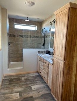 Accessible bathroom with walk-in shower, wood vanity, tile walls, and wood-look flooring