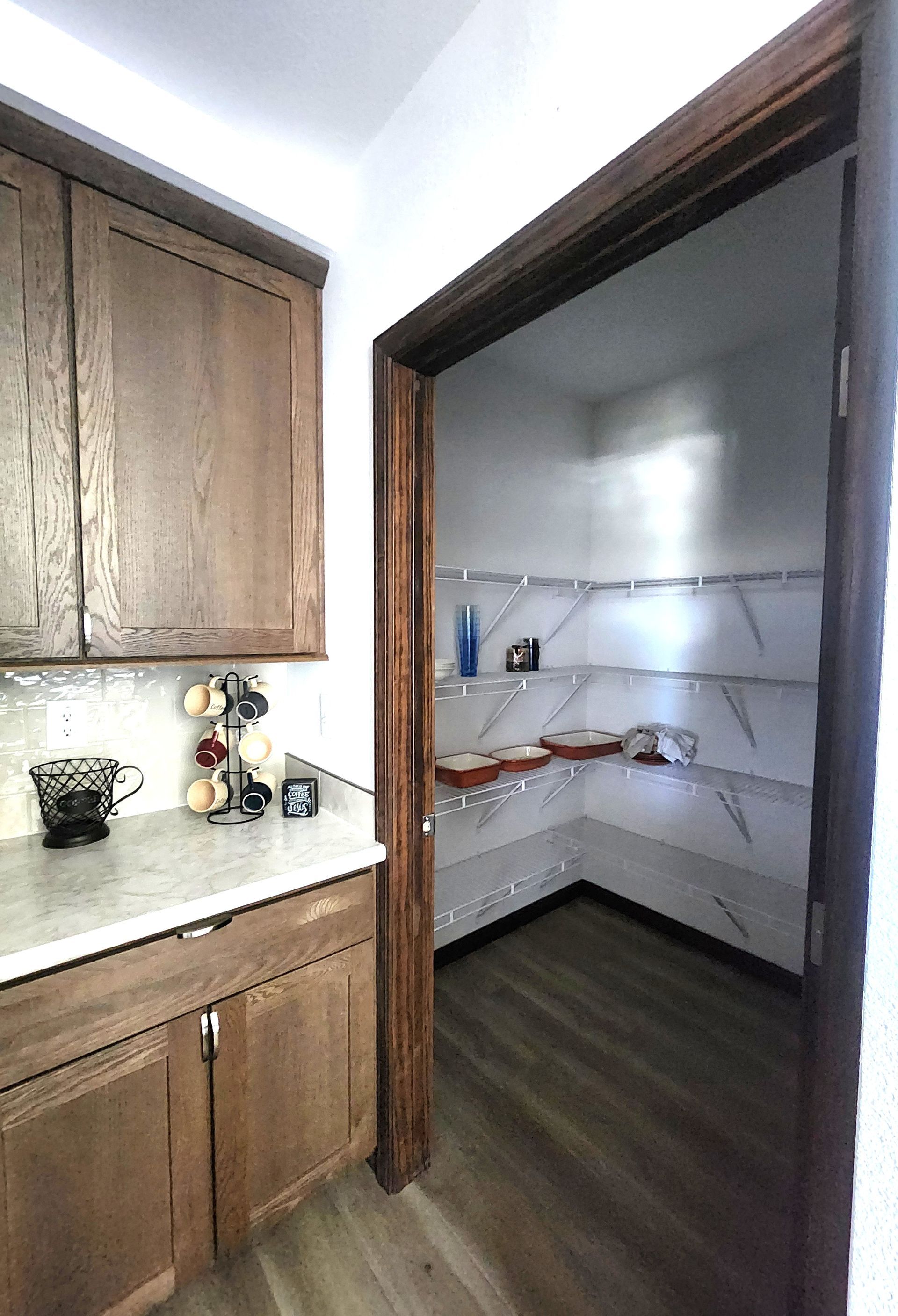 Small kitchen with wooden cabinets and an open pantry shelf with dishes and wire racks.