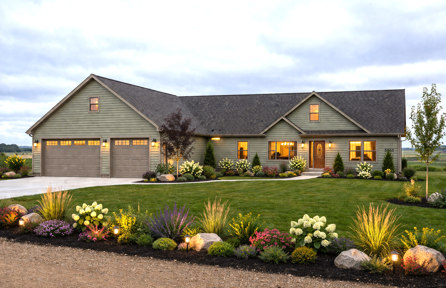 Suburban house at dusk with warm lights, two-car garage, and landscaped flower beds