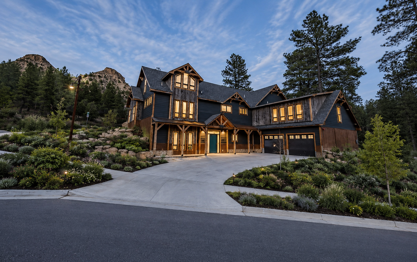 Large modern mountain home with warm lights, stone accents, and a curved driveway at dusk