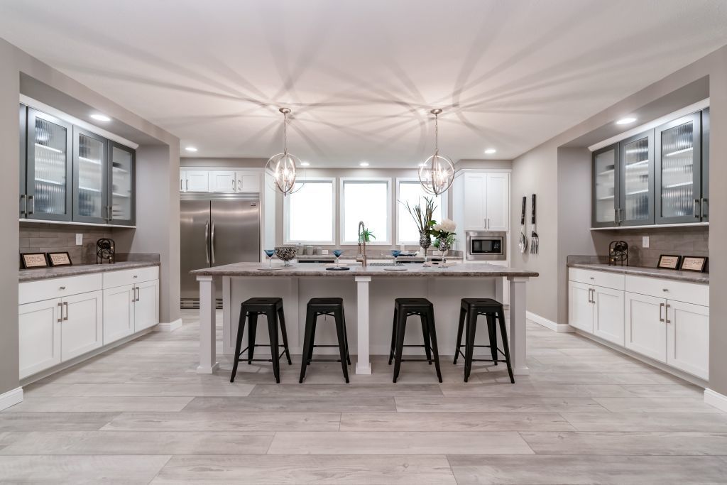 Bright modern kitchen with a large island, black stools, white cabinets, and stainless steel appliances.