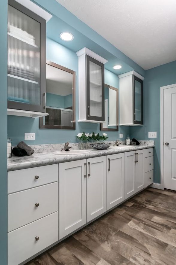 Bright bathroom with white cabinets, marble countertop, blue walls, mirrors, and wood-look floor.