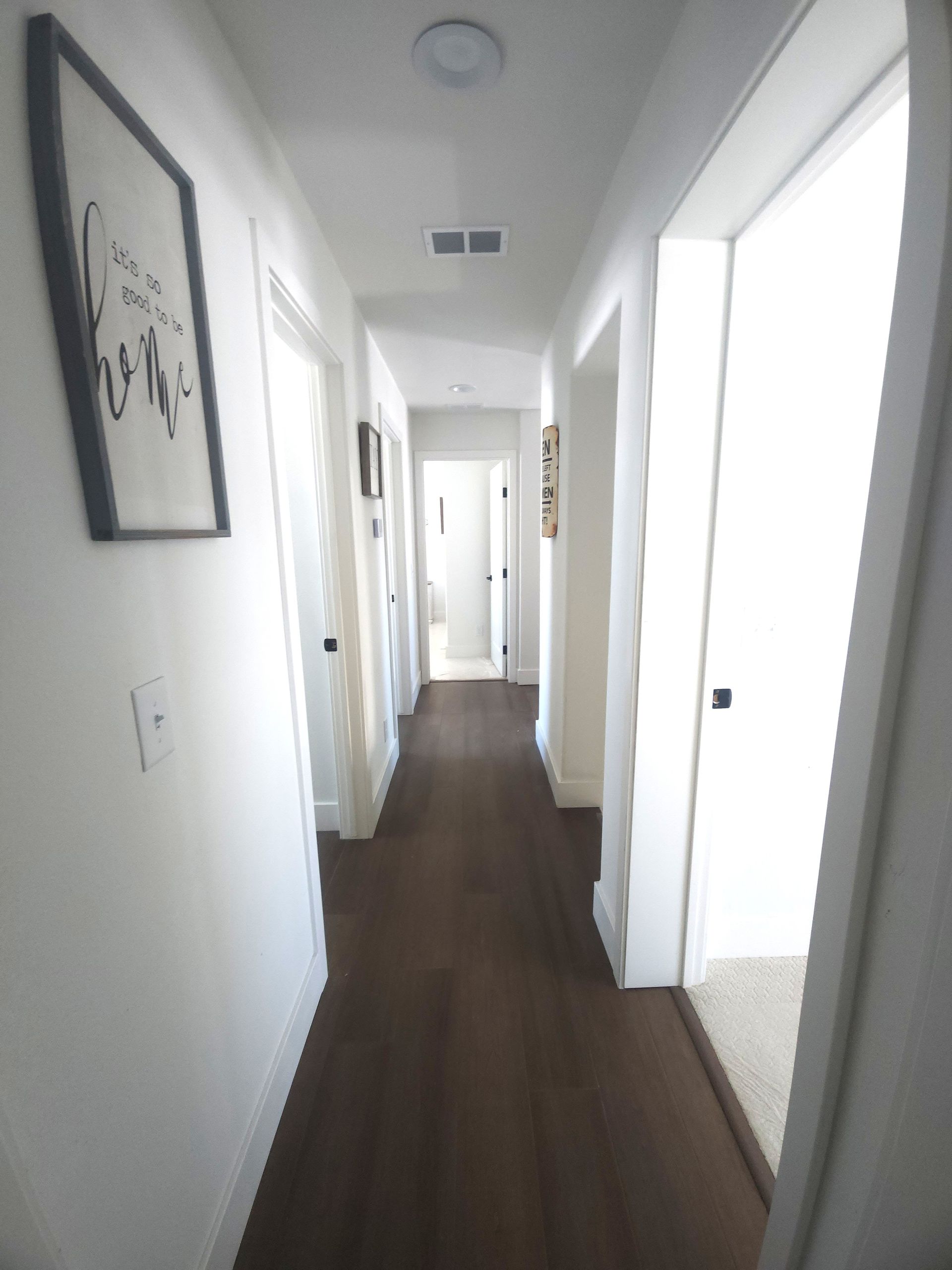 Narrow white hallway with wood floors, doors on both sides, and framed wall art.