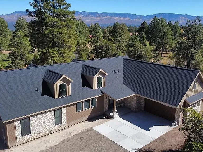 Aerial view of a house with dark gray roof, beige brick walls, and mountain scenery behind it