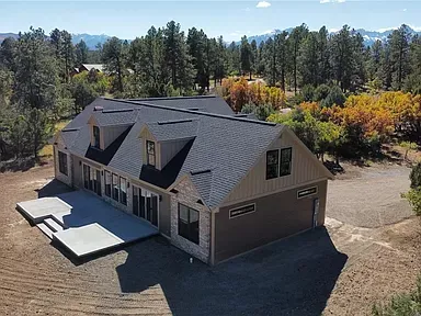 Aerial view of a modern dark-roofed house surrounded by trees and open land.