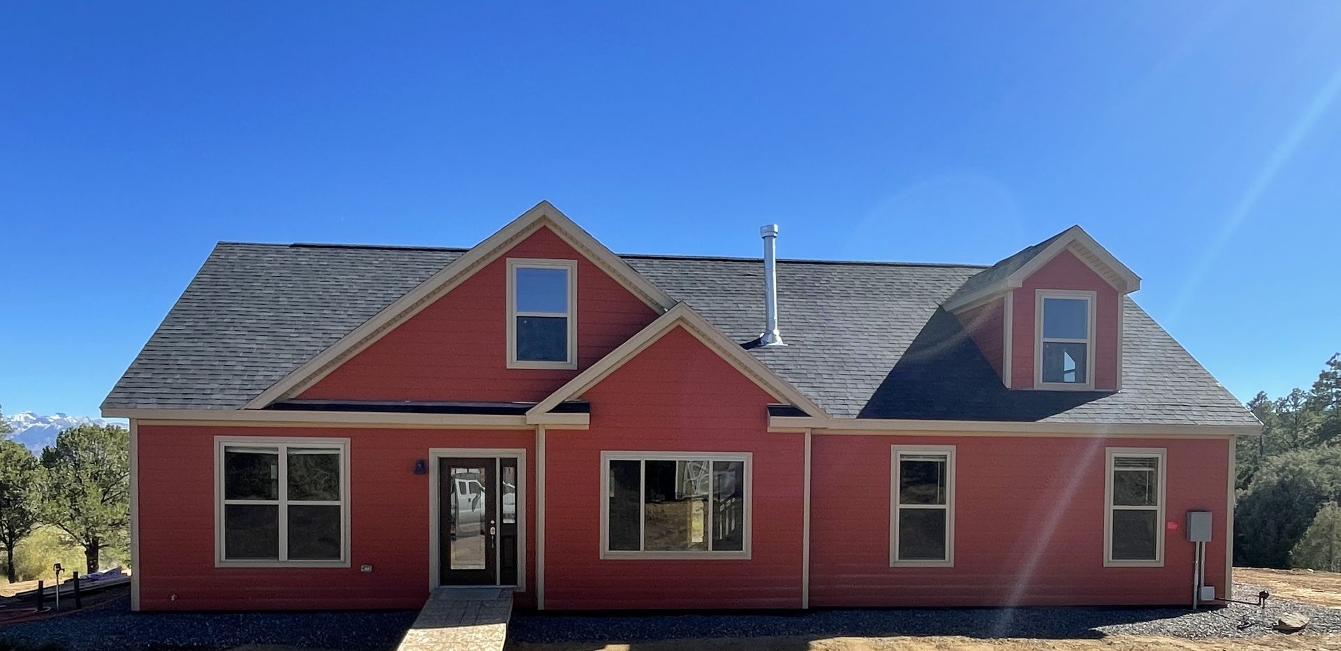 Red house with gray roof and dormer windows under a clear blue sky