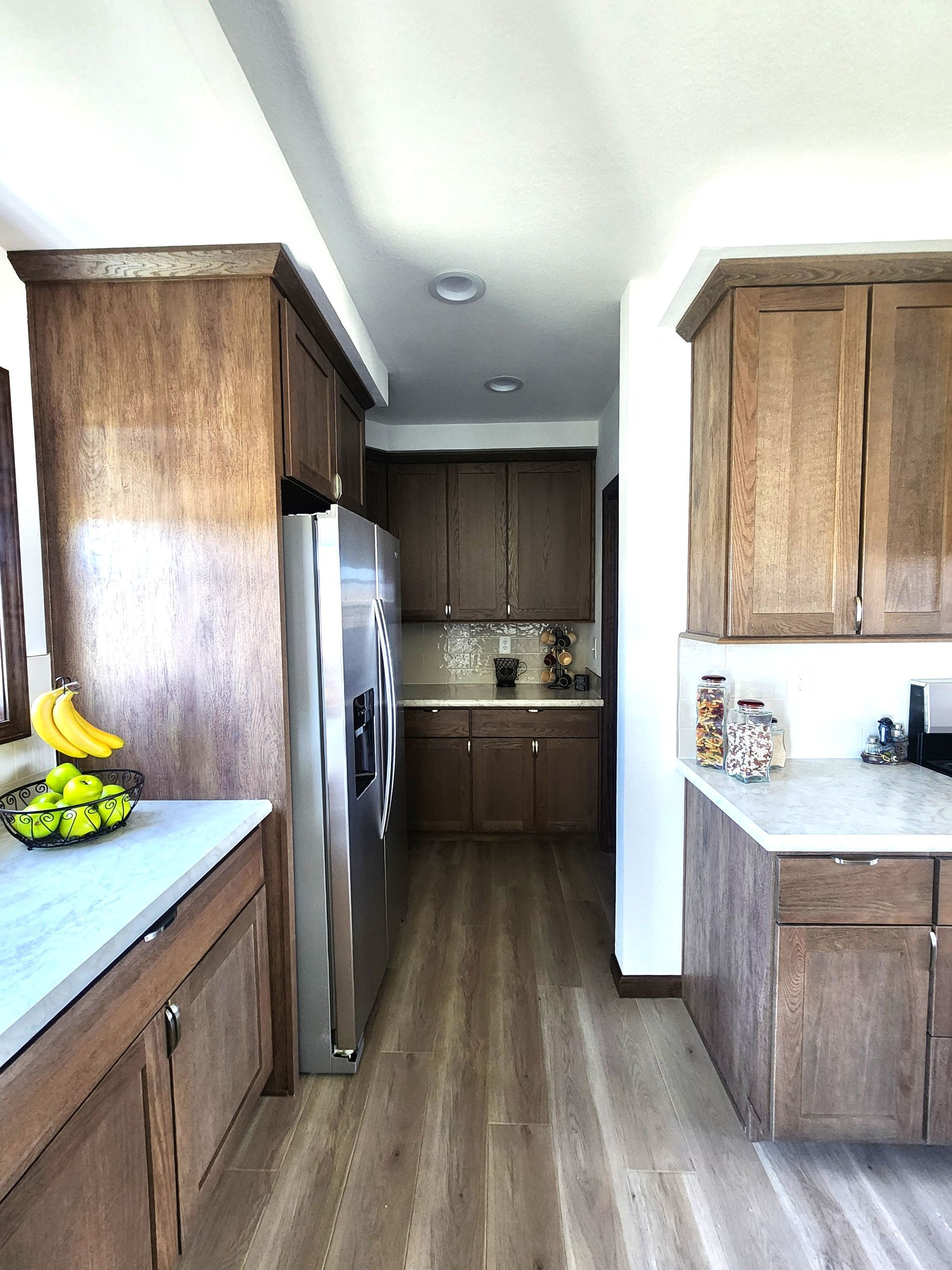 Bright kitchen with wood cabinets, stainless fridge, white countertops, and bananas on the left counter.