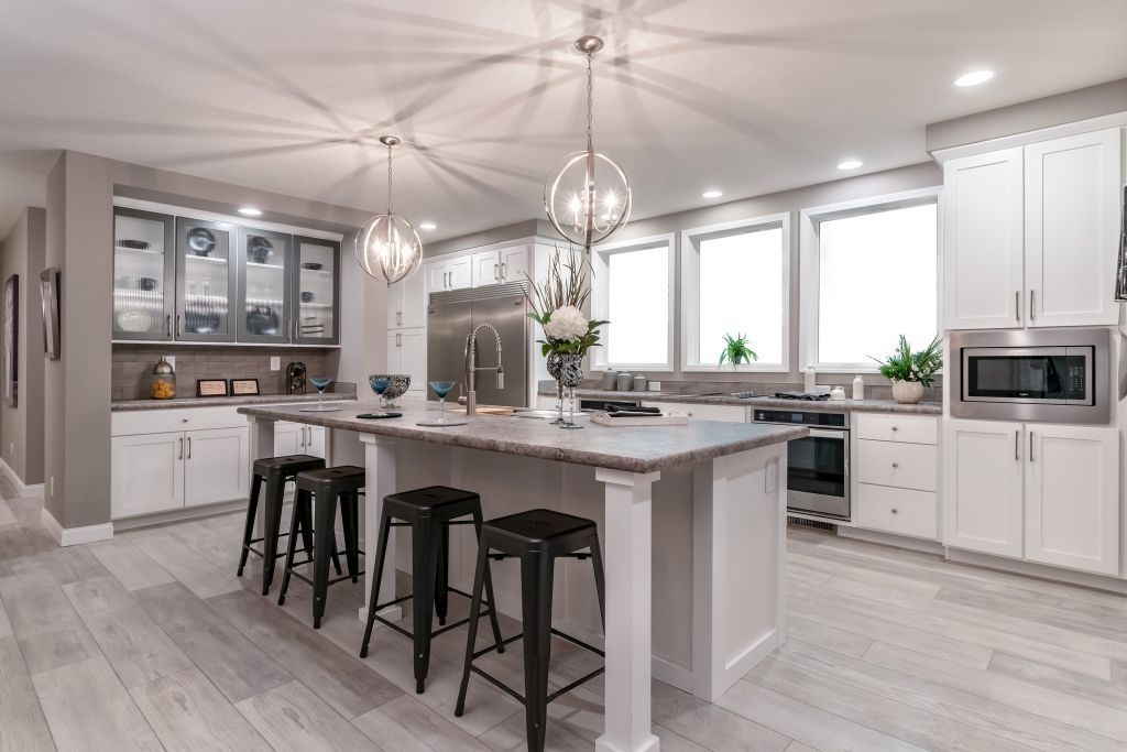 Bright modern kitchen with white cabinets, a large island, black stools, and pendant lights
