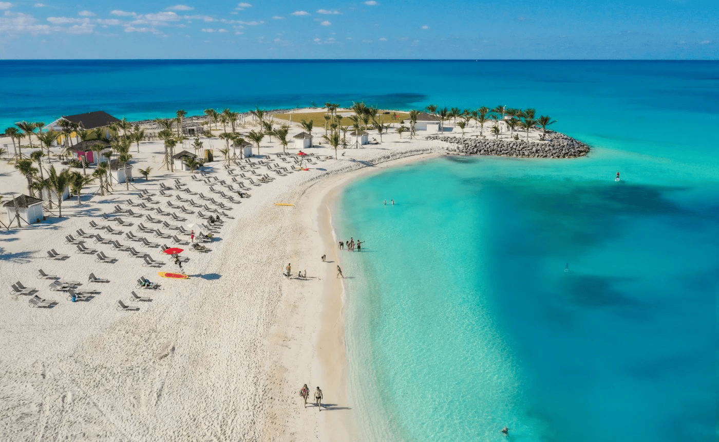 Beach with white sand, turquoise water, and palm trees under a blue sky; people walk and relax.