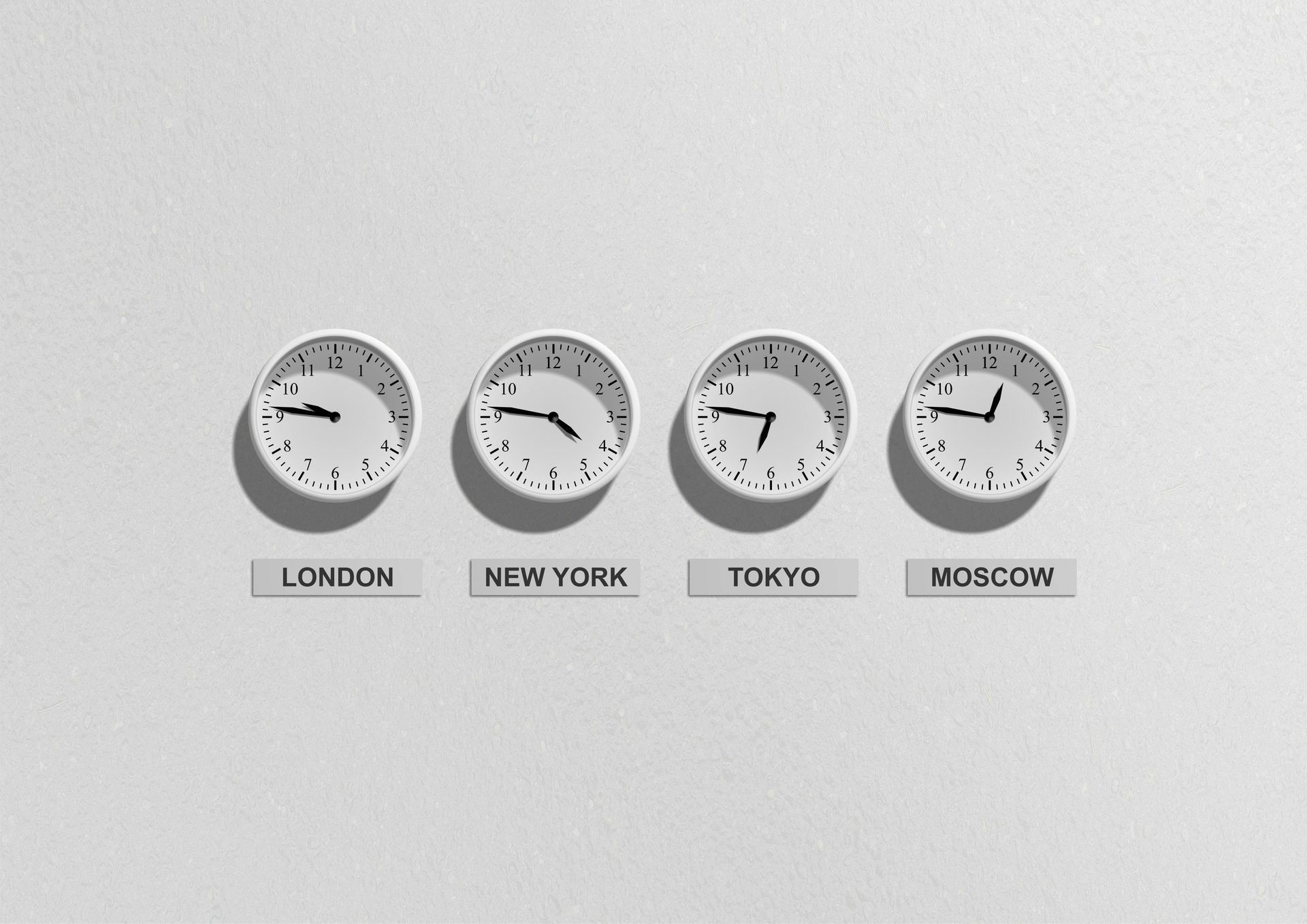 Four clocks displaying times for London, New York, Tokyo, and Moscow, mounted on a white wall.