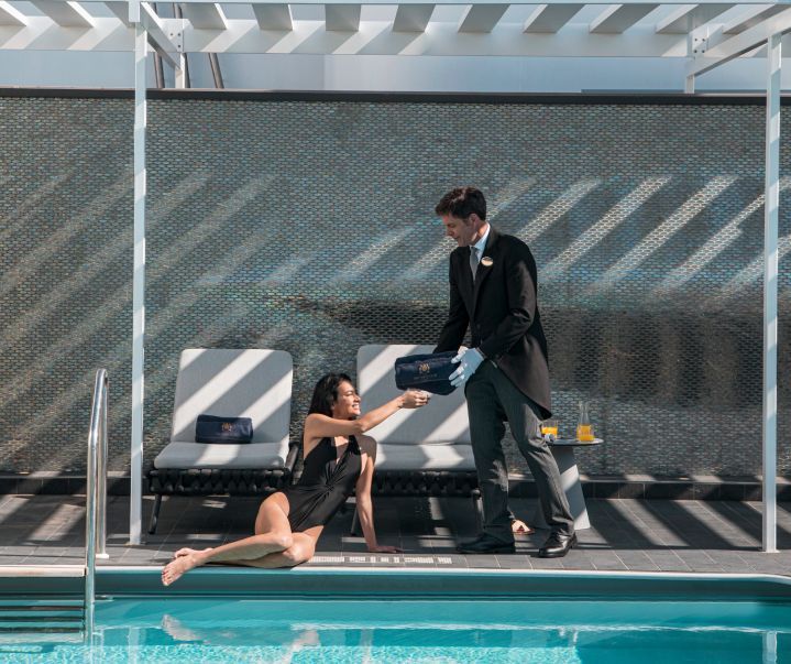 Woman by pool receives item from attendant. Poolside setting, blue water.