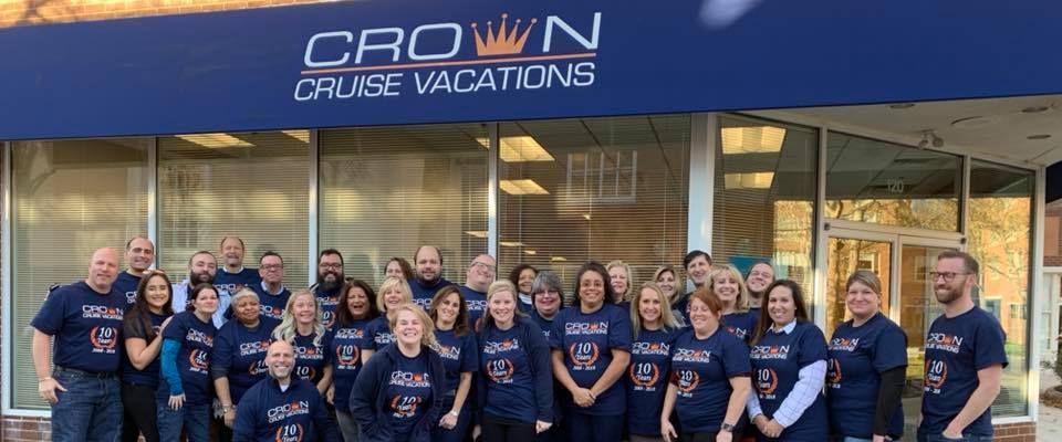 A group of people wearing matching shirts pose in front of a Crown Cruise Vacations storefront.