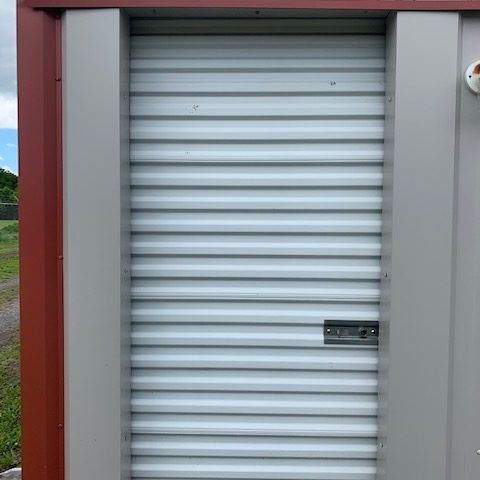 Closed white roller shutter door with a small handle in a gray and red frame