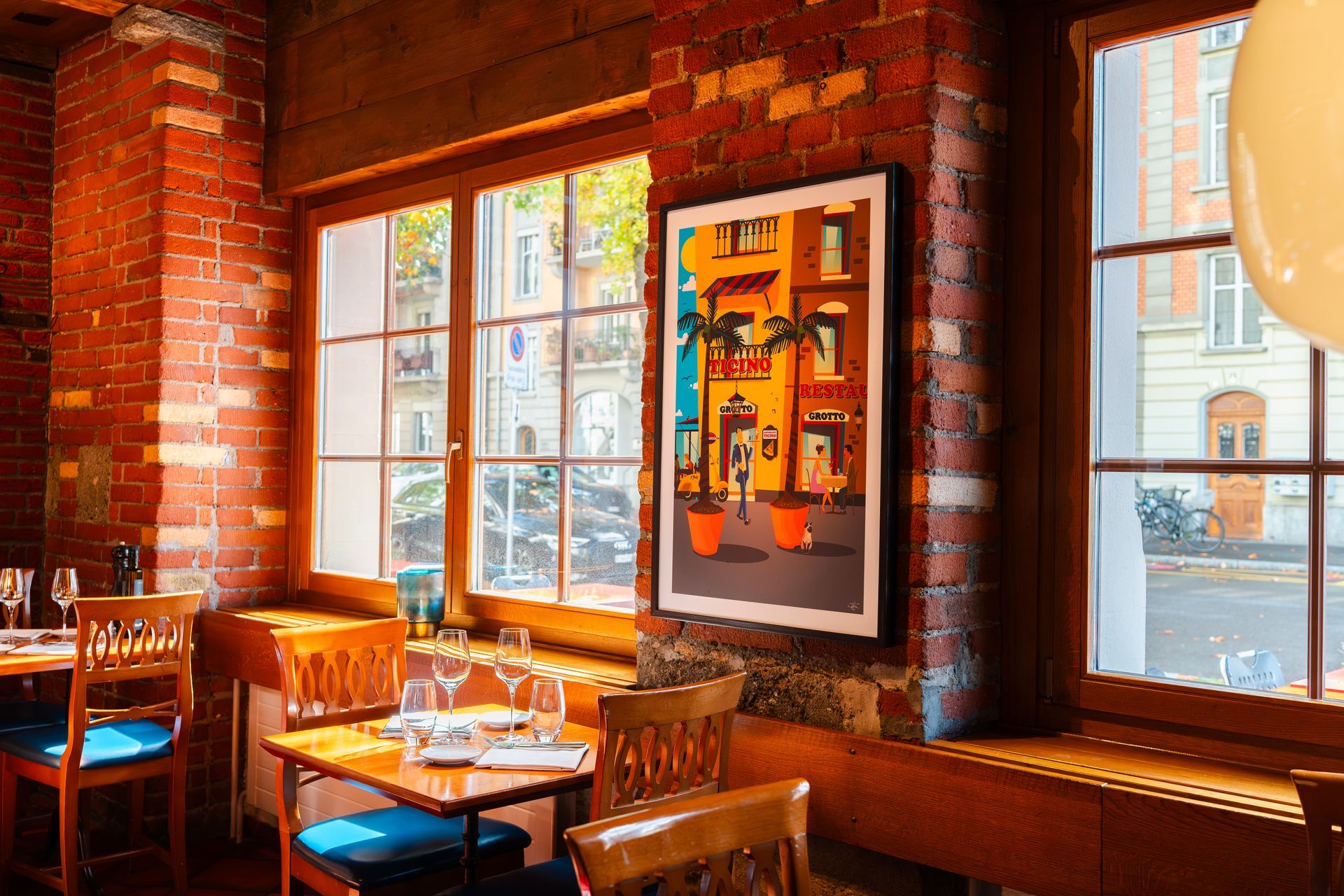 Gemütliches Café mit Backsteinwänden, Holztischen und -stühlen, großen Fenstern und farbenfrohen gerahmten Kunstwerken an der Wand