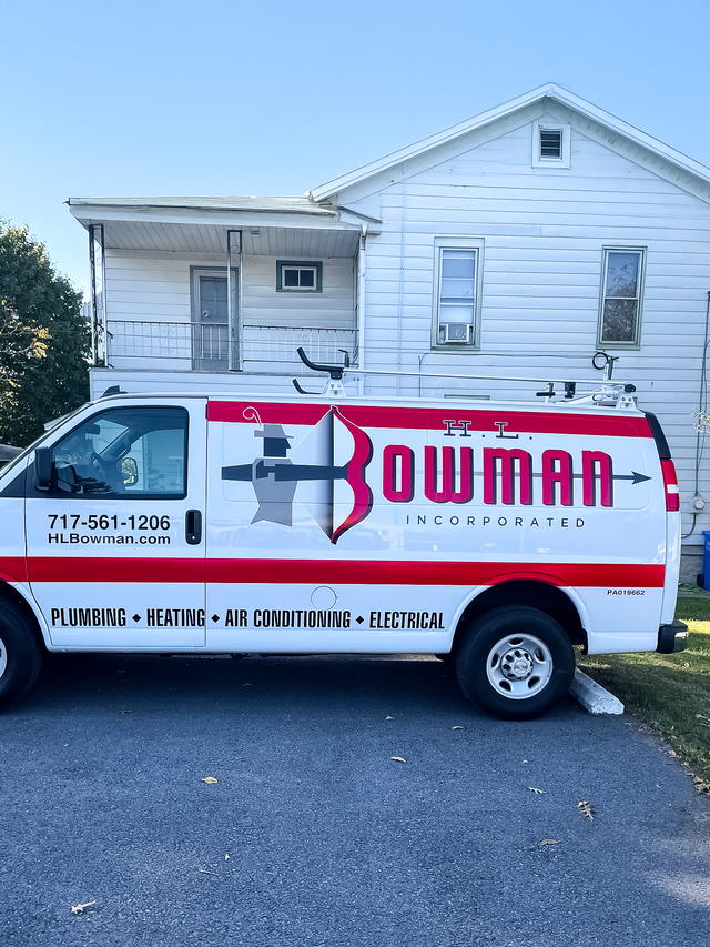 White plumbing service van with red logo parked in front of a white house.