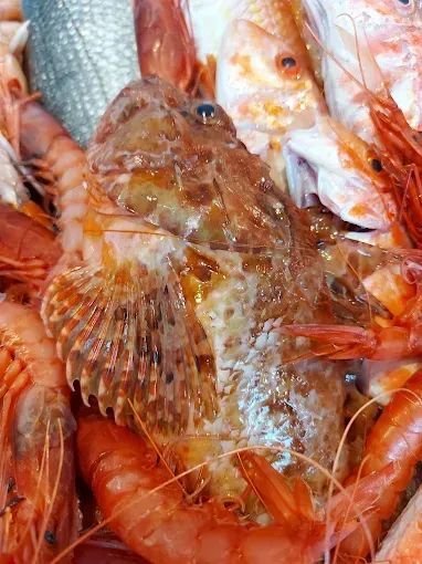 Primo piano di frutti di mare cotti assortiti, tra cui gamberi e pesce, ammucchiati insieme con tonalità arancioni e argentate