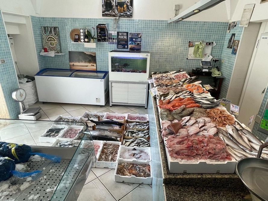 Bancarella di pesce al coperto con pesce esposto sul ghiaccio e vassoi di frutti di mare sui tavoli.