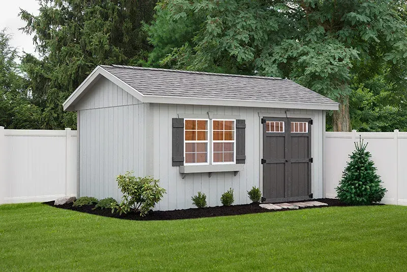 Light blue shed with dark gray door, window, and roof. Green grass and shrubs in a backyard.