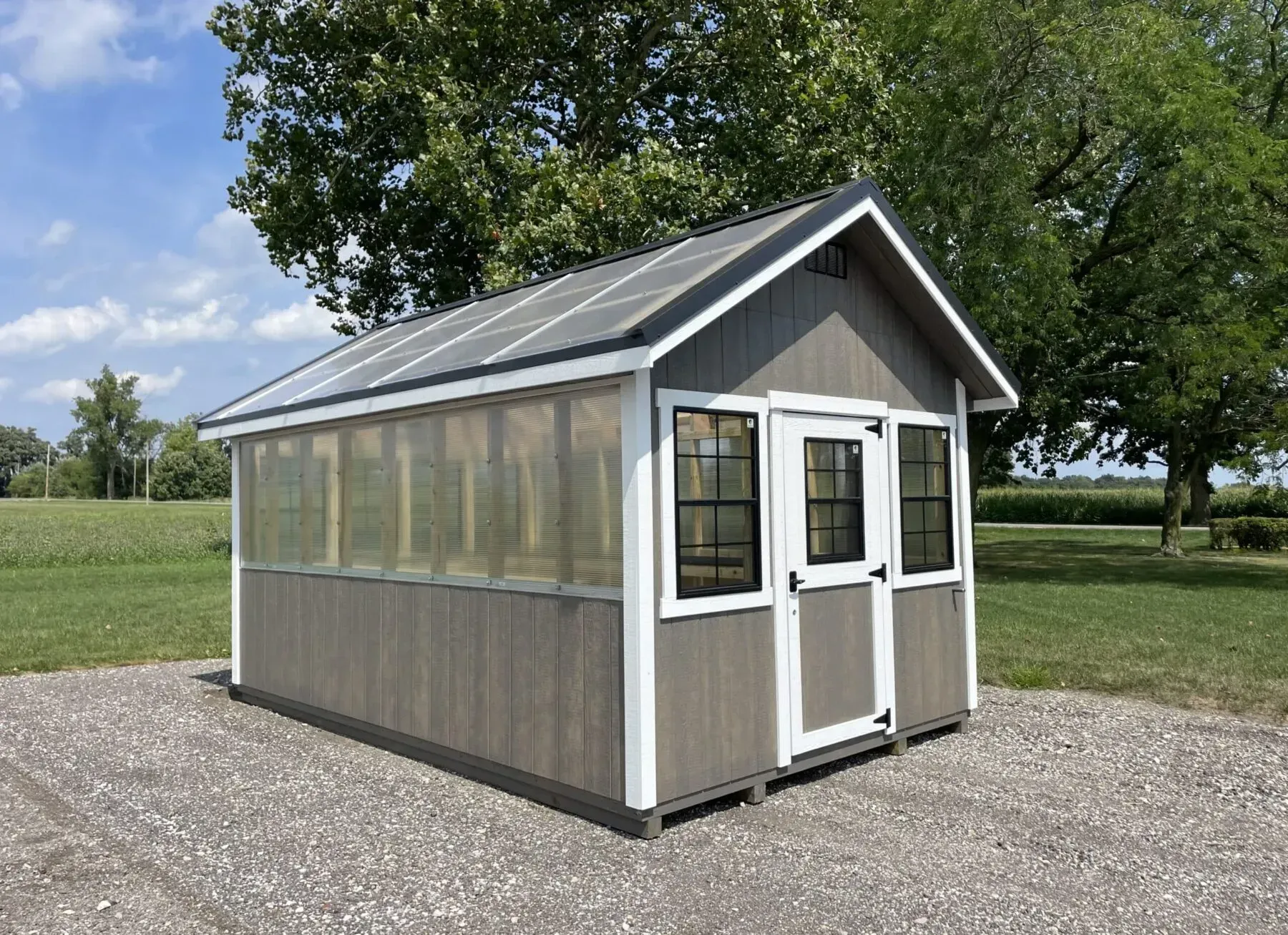 Gray Greenhouse with transparent panels, white trim, and a black roof, set on gravel.