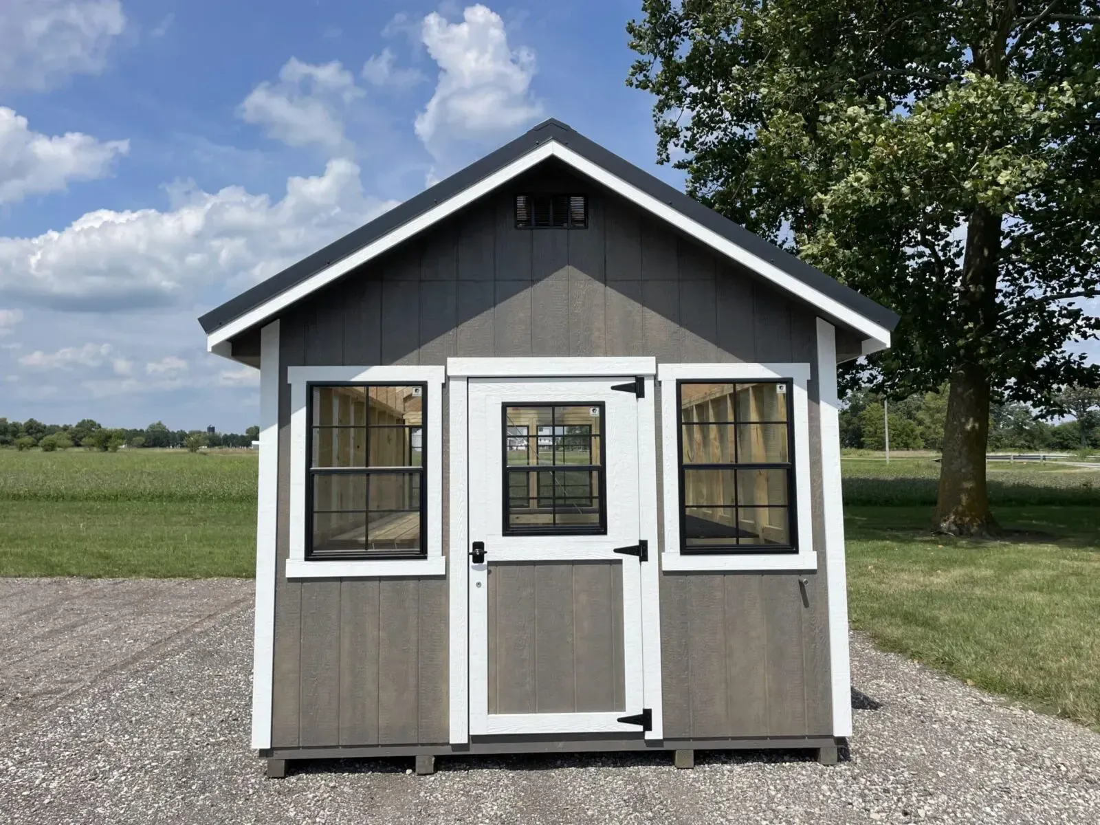 Gray and white greenhouse with black window and door frames; set in a grassy area under a blue sky.