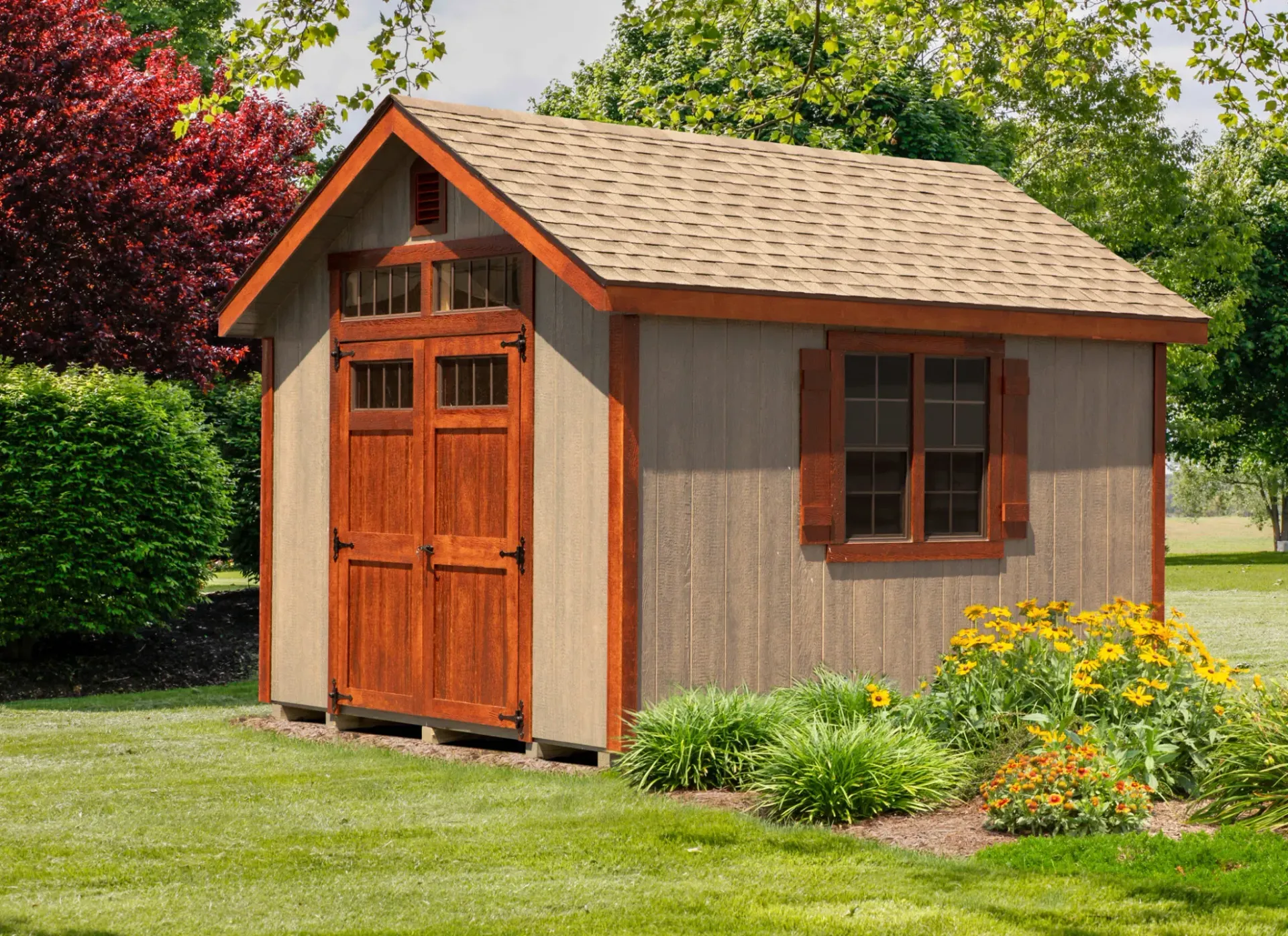 Wooden garden shed with brown doors and window, surrounded by flowers and greenery.
