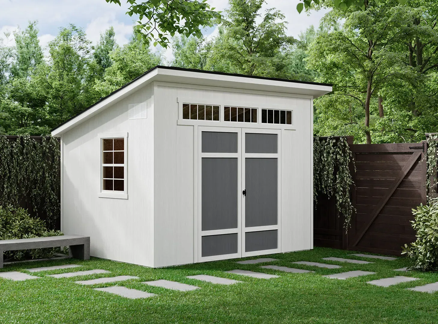 White shed with black roof, double doors, window. Located in a yard with trees, pavers, and a bench.