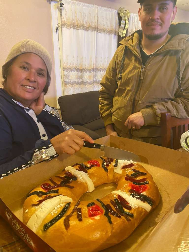 Two people prepare to slice a decorative Rosca de Reyes bread in a casual home setting.